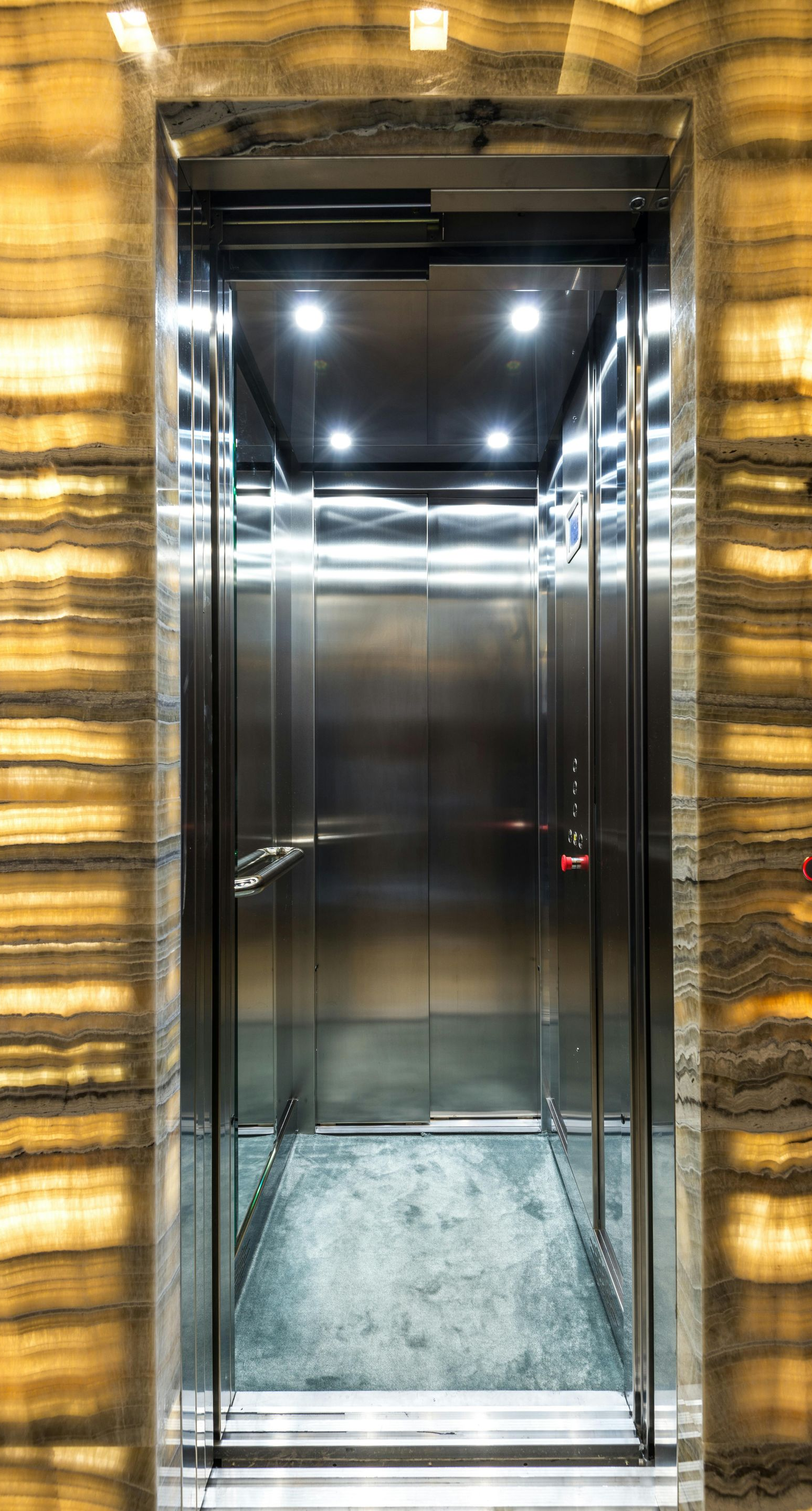 An elevator with open doors, stainless steel interior, and marble-like wall surround.