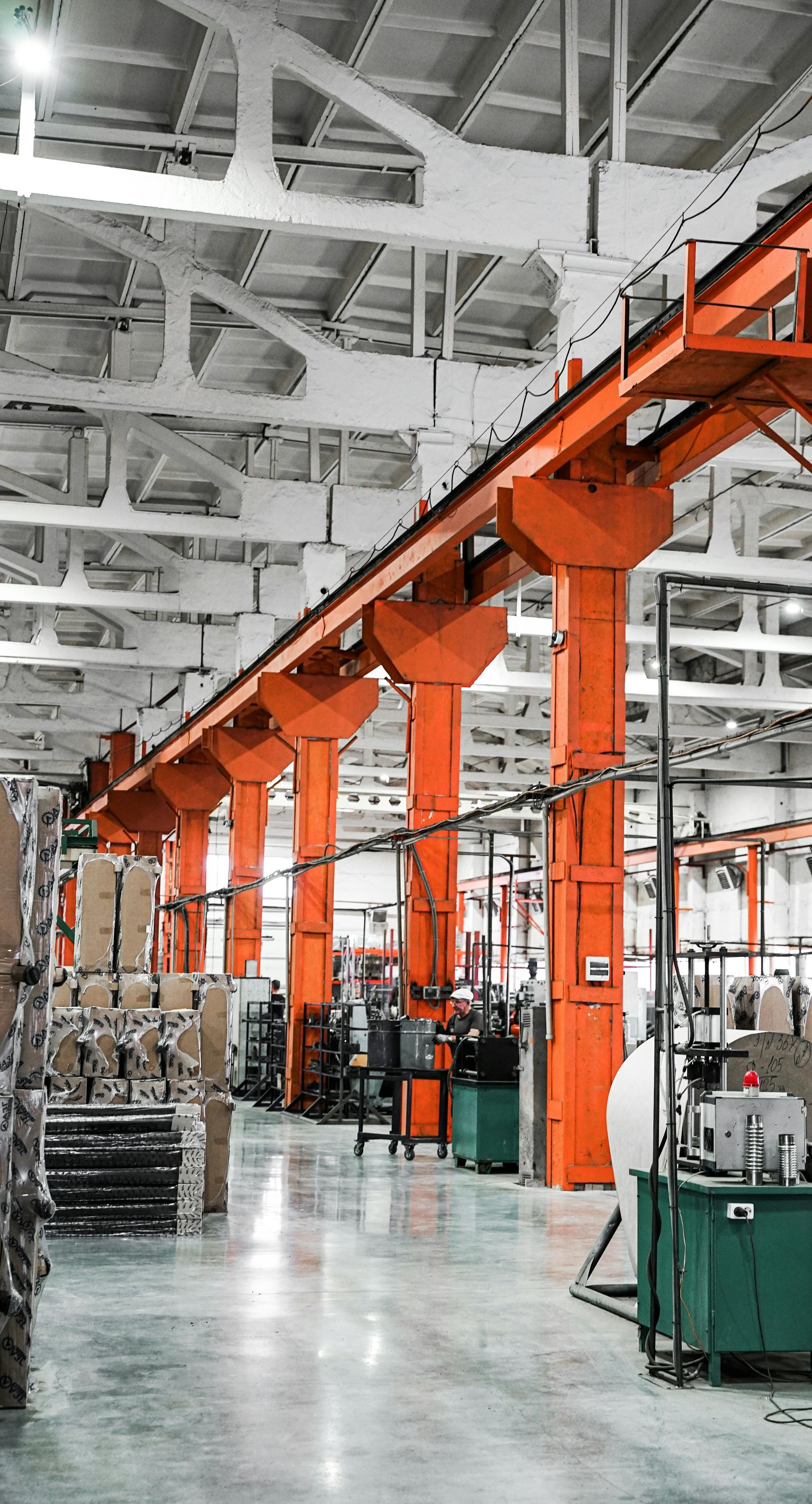 A long, industrial warehouse interior featuring a row of tall orange metal columns supporting an overhead structure.