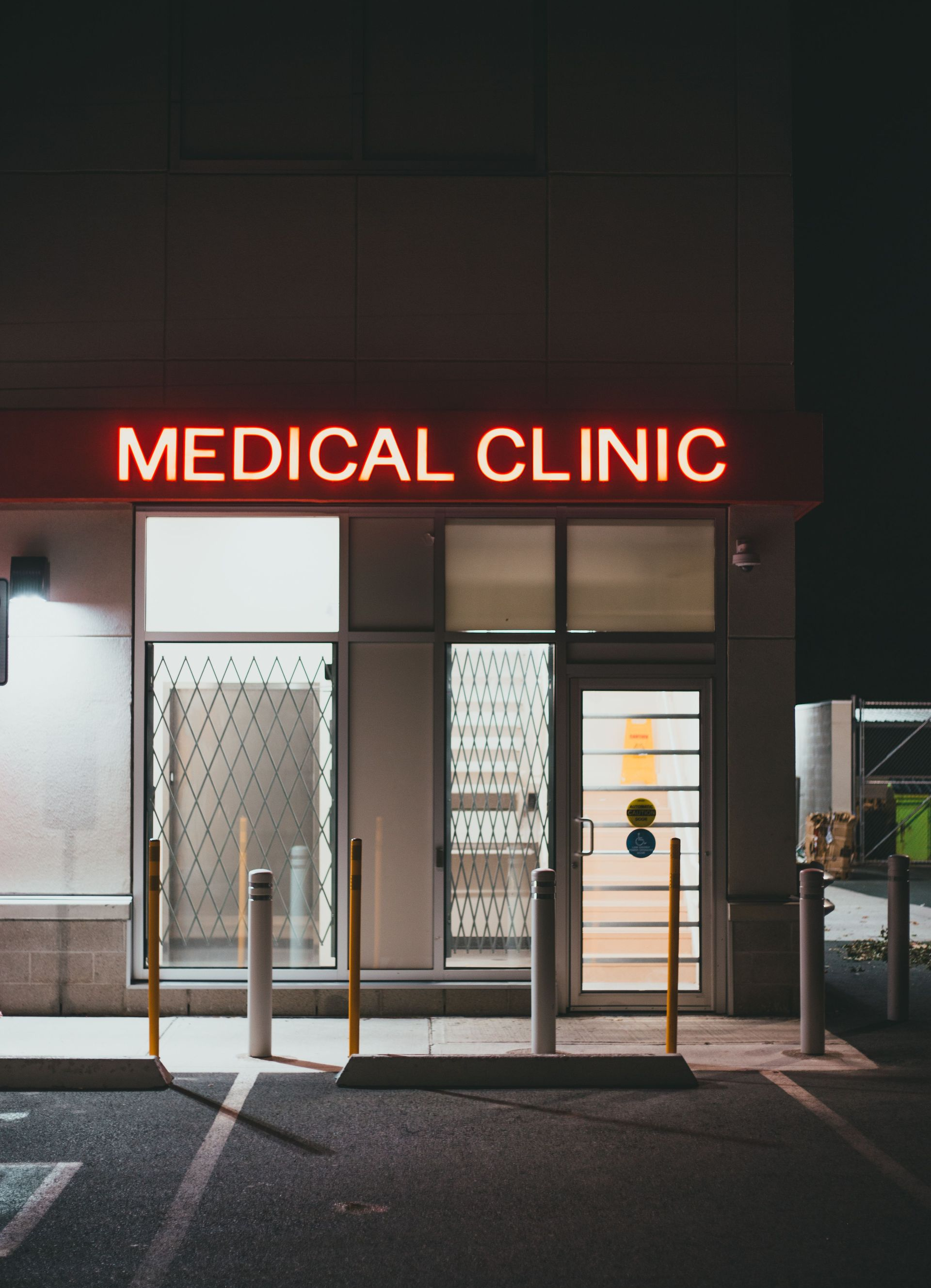 Nighttime exterior of a medical clinic with a red neon sign and glass entrance