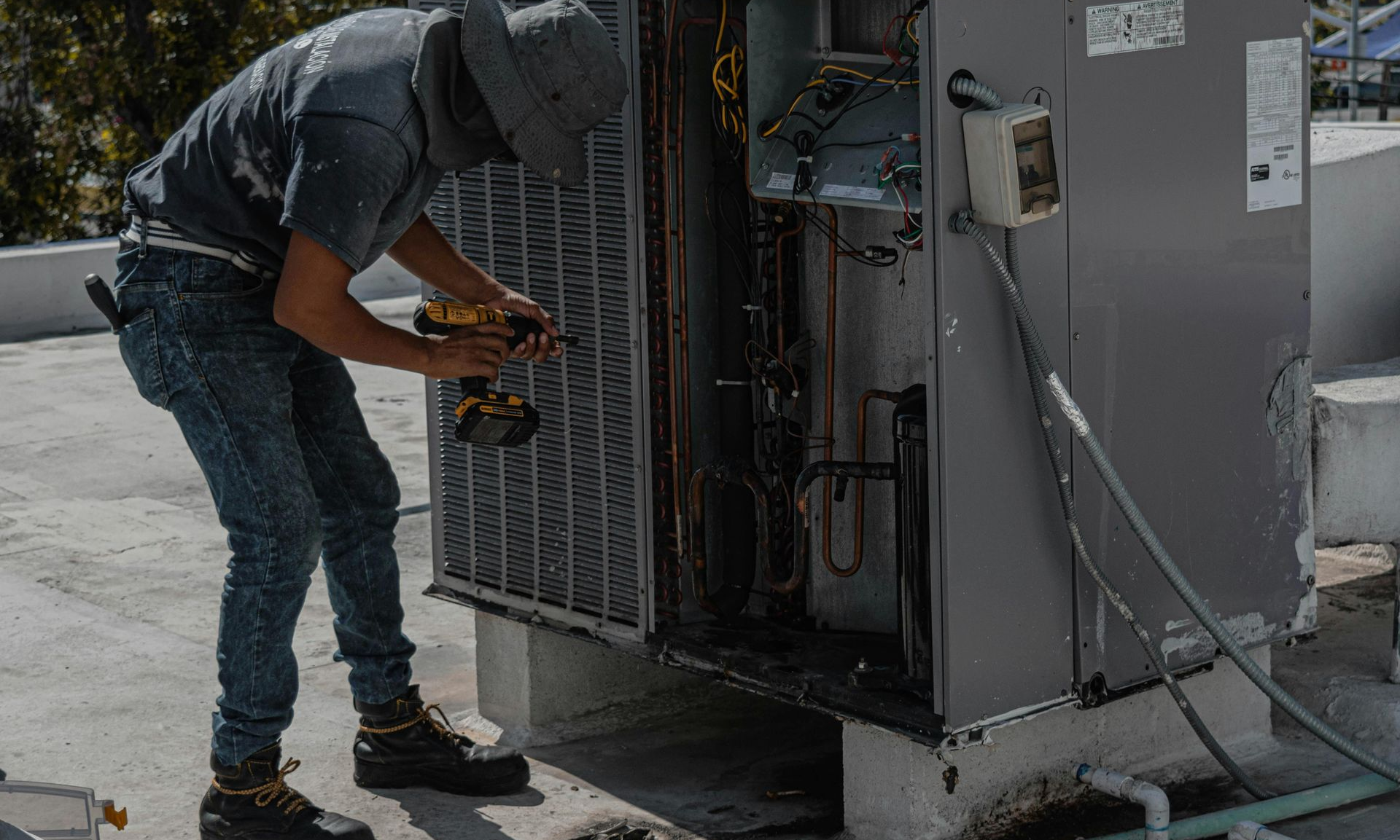 Technician repairing rooftop HVAC unit with tools, next to open metal panels and visible wiring.