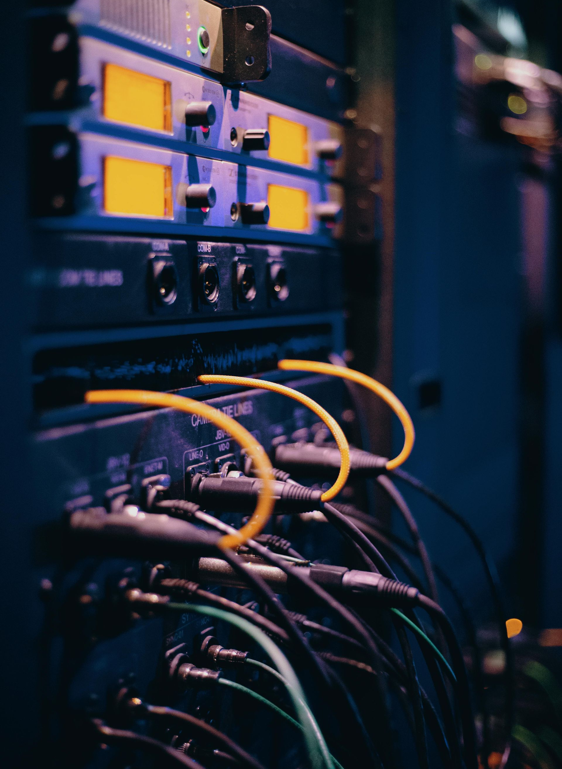 A vertical rack of electronic equipment with glowing yellow displays and multiple black cables connected to it.