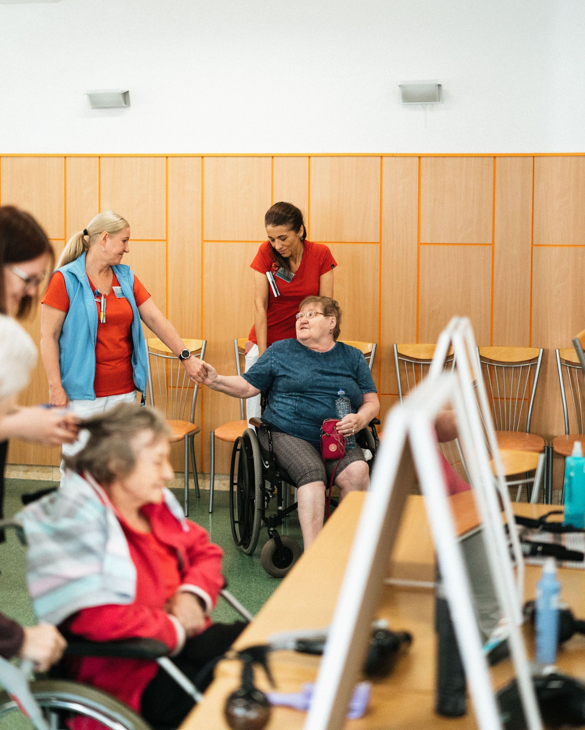 People in a rehab gym assisting a person in a wheelchair, with exercise equipment and mirrors in the background.