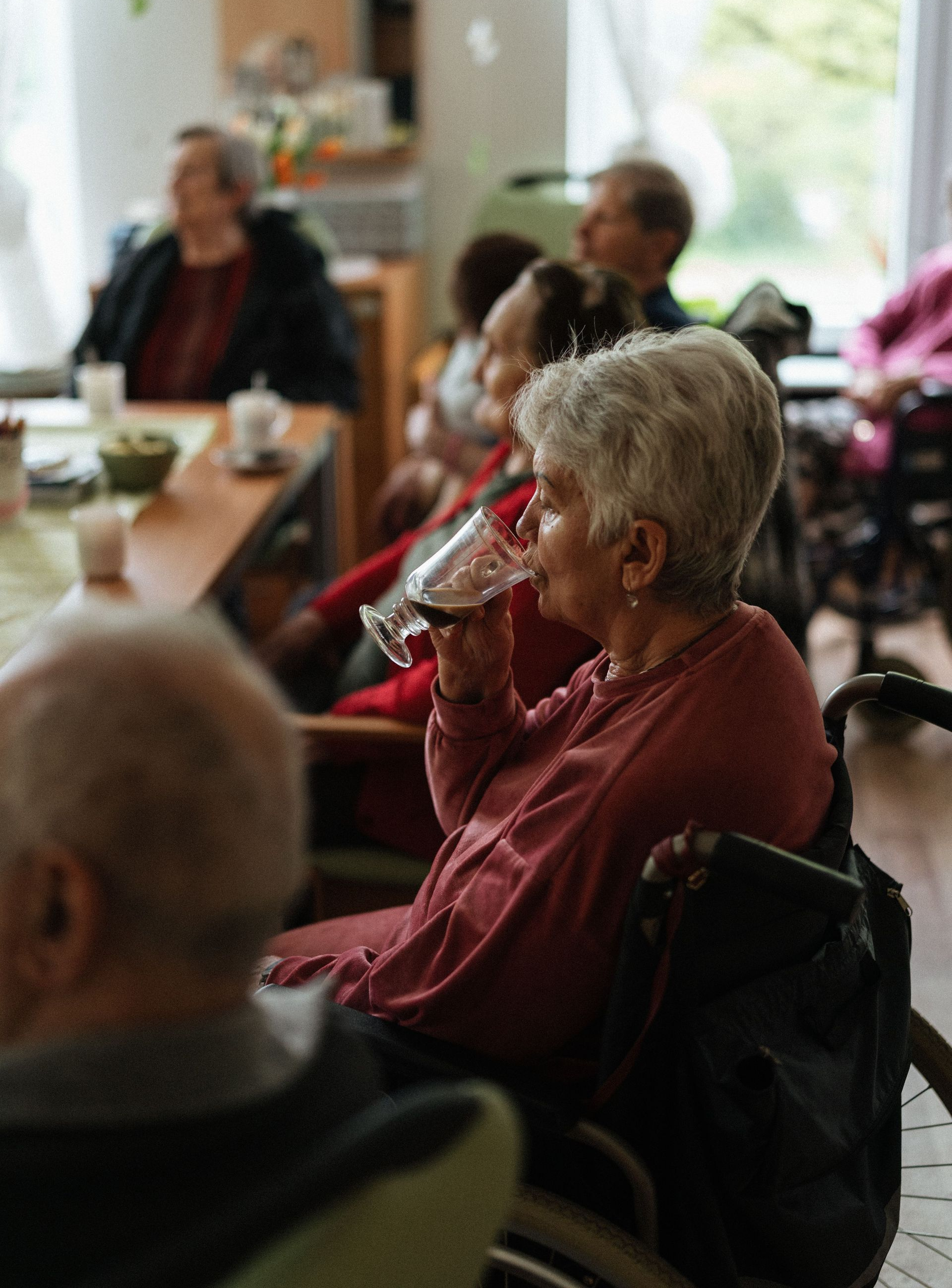 People seated in a café, one elderly person in a red sweater drinking water.