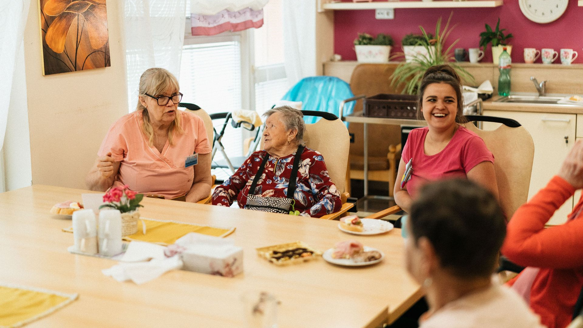 People sitting around a table in a bright room, sharing snacks and talking