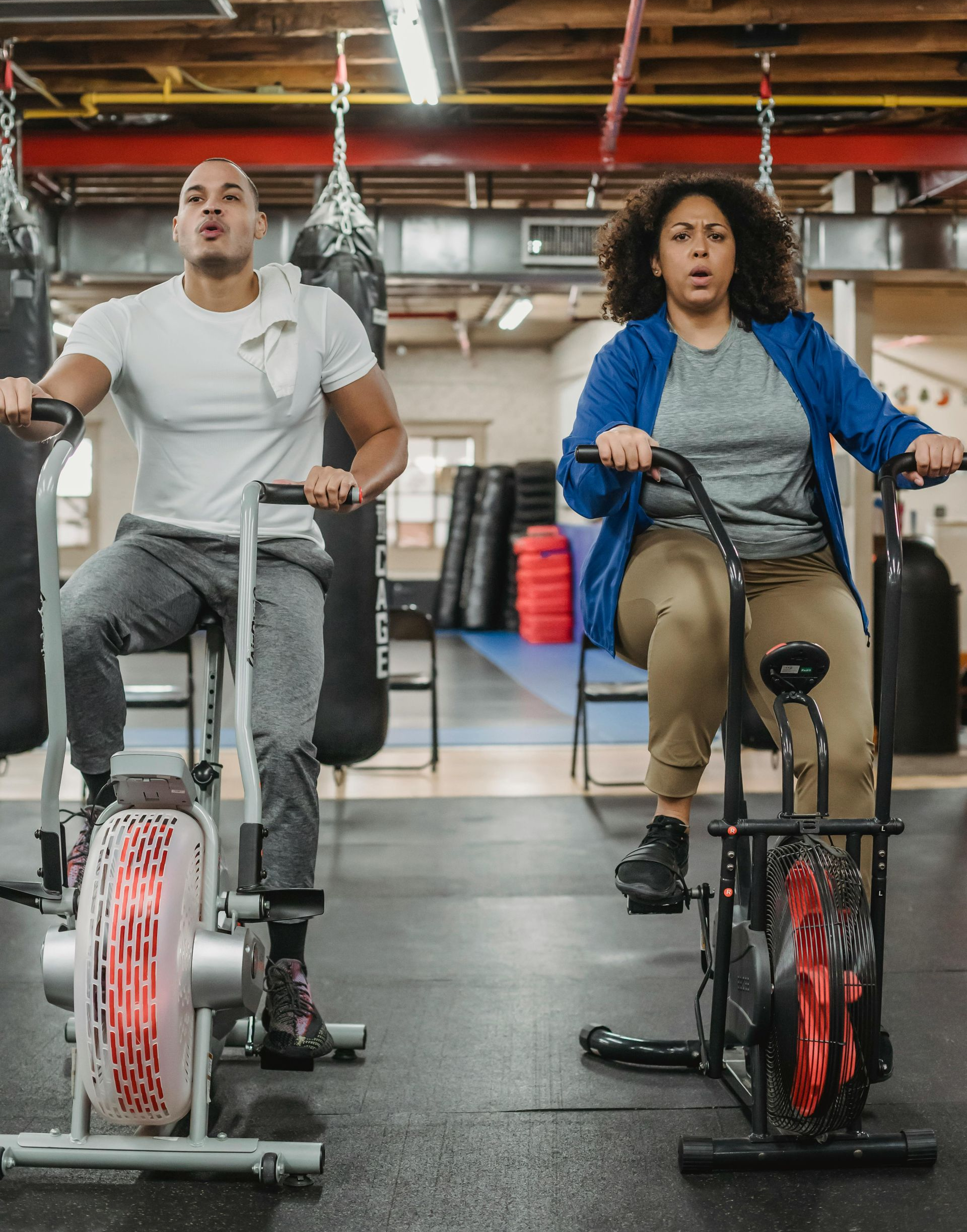 Two people exercising on stationary air bikes in a gym.