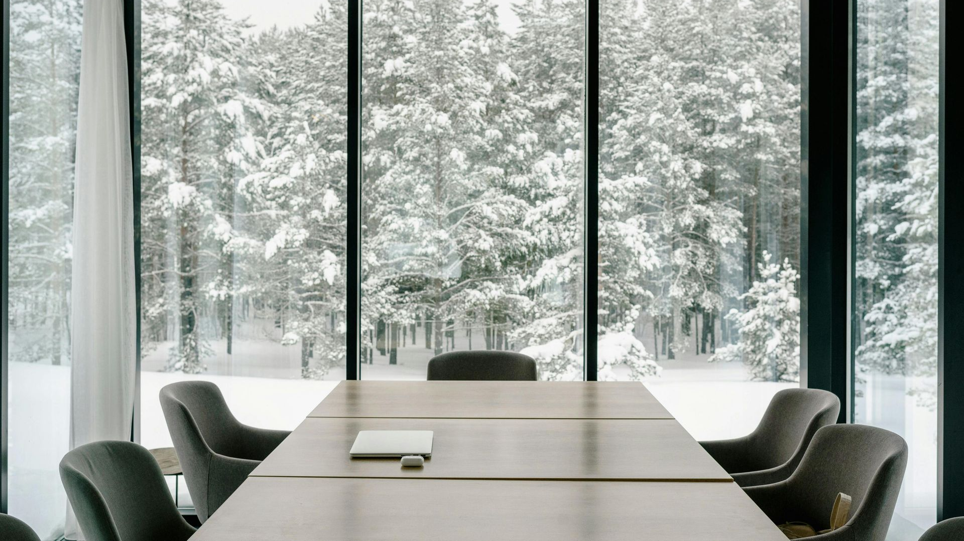 Modern conference room with a long table and chairs overlooking snowy trees through floor-to-ceiling windows