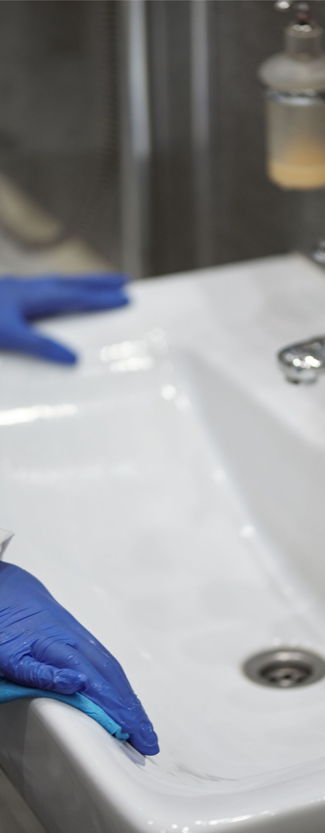 Blue-gloved hands cleaning a white sink at a lab or clinic workstation