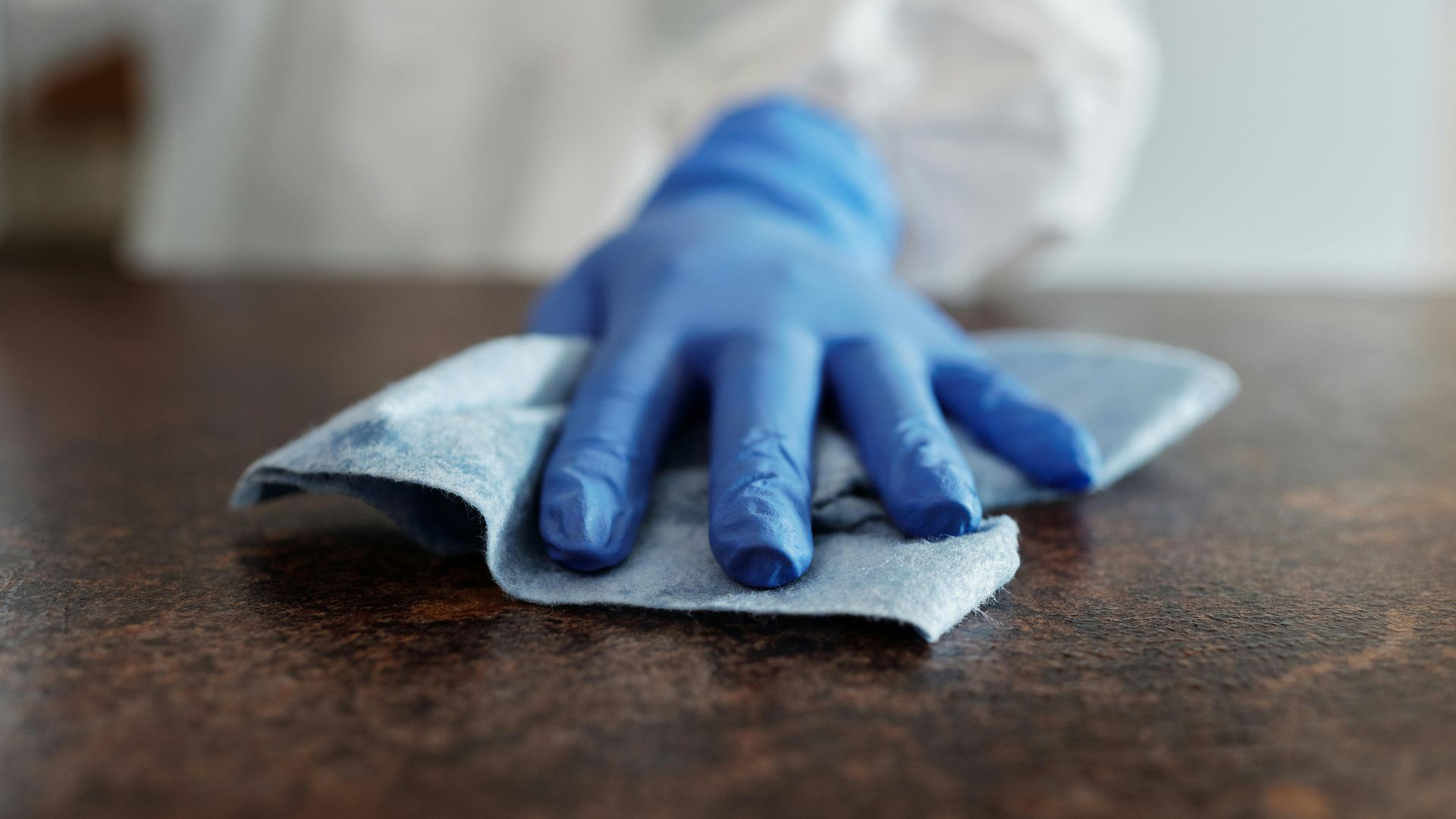 Blue-gloved hand wiping a brown countertop with a blue cloth.