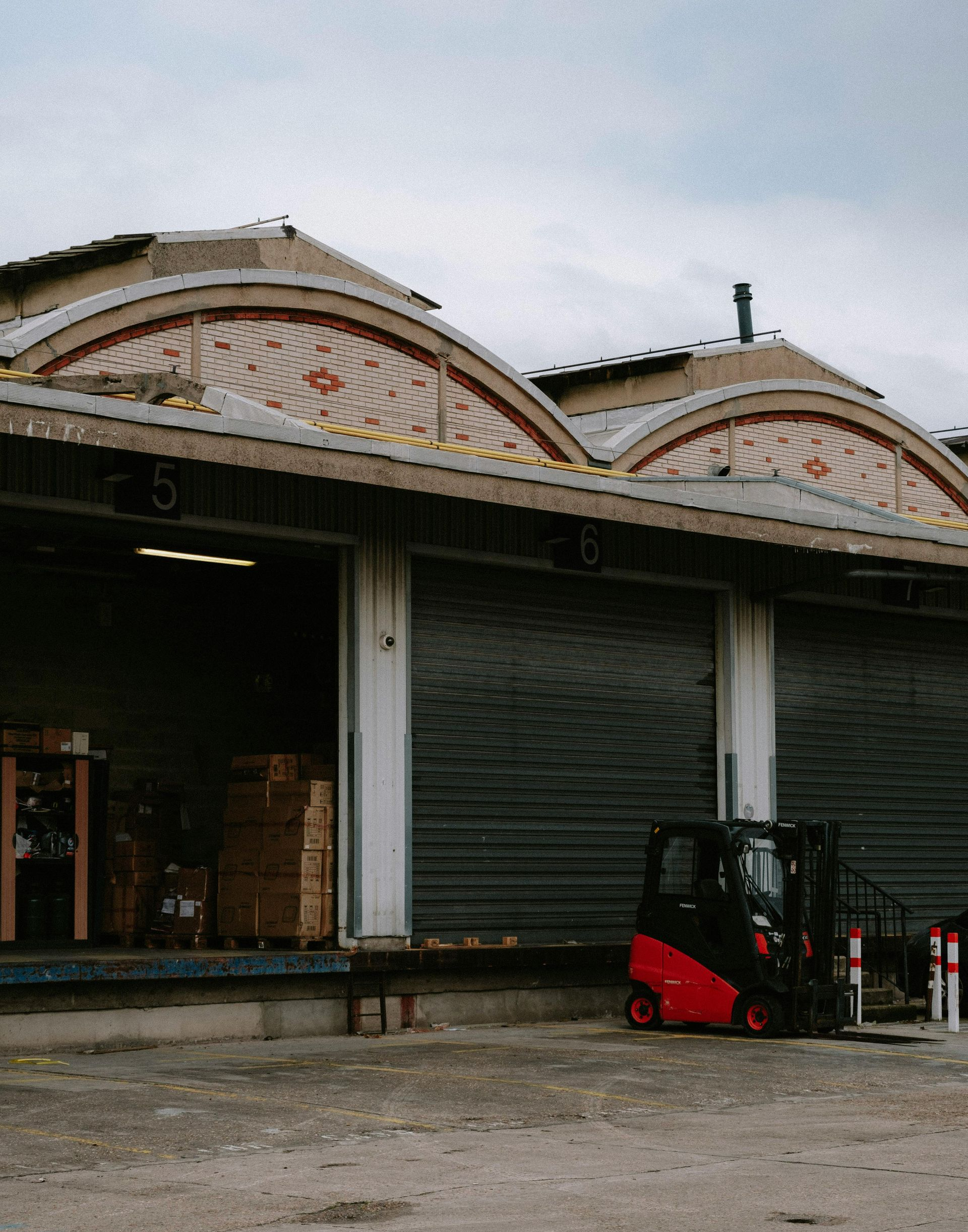 A red forklift parked outside a warehouse with arched roof details and open loading bays.
