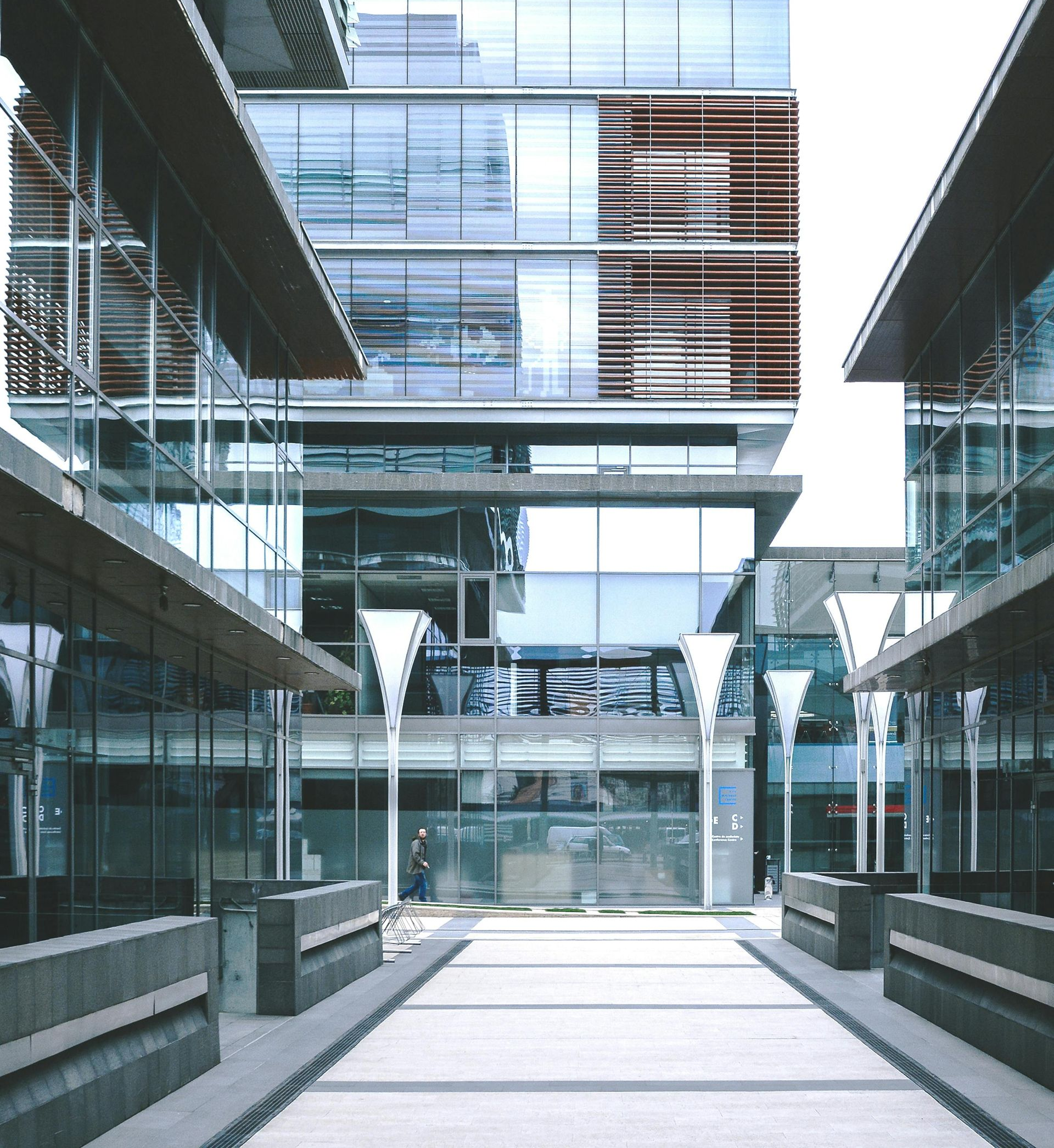 Modern glass and steel office buildings in an urban setting; a walkway leads toward the central tower.