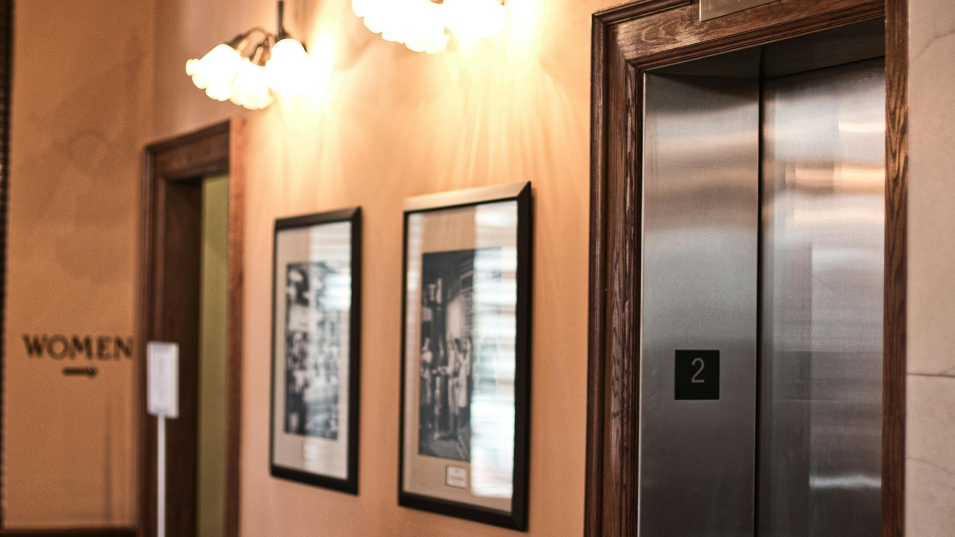 Elevator and hallway with framed art, sconces, and a 