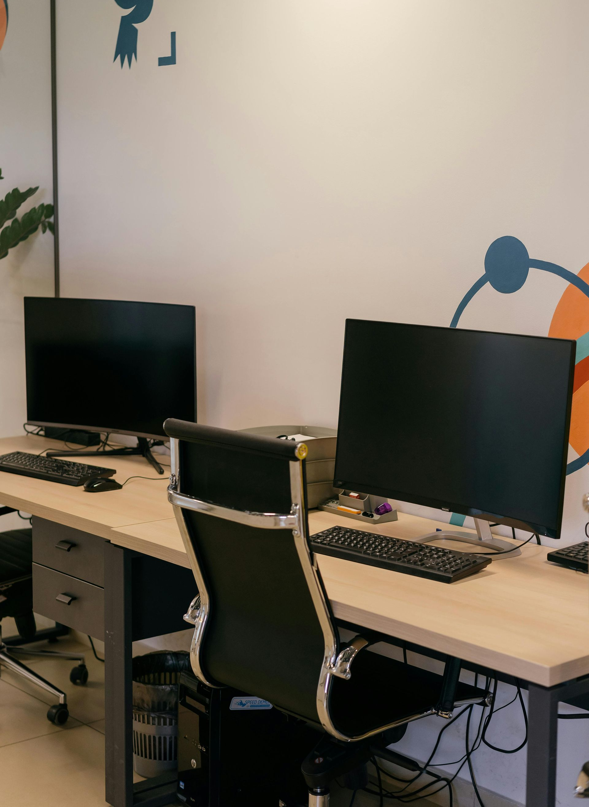 Office desk with two monitors, a chair, and cables against a beige wall.