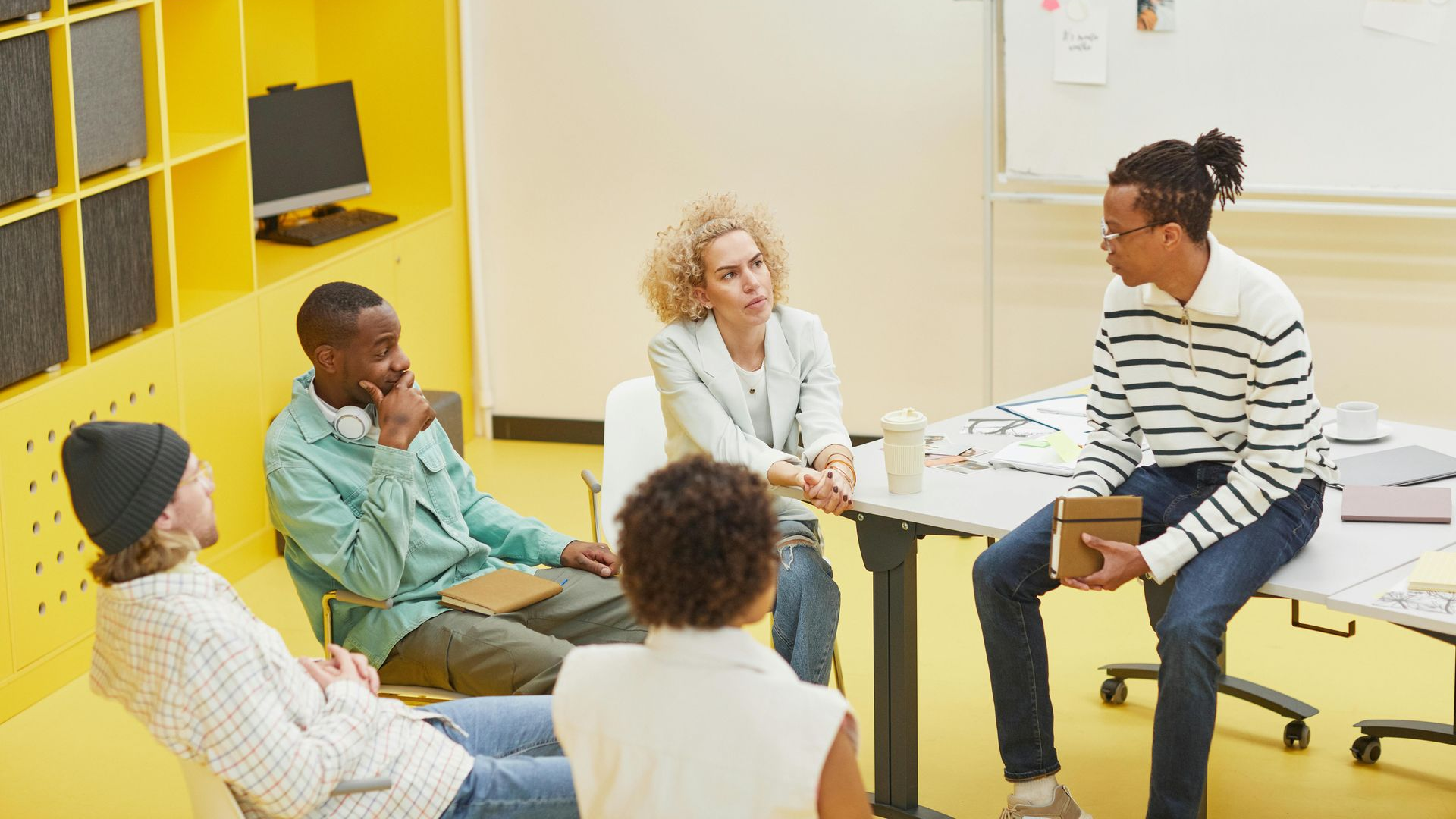Small group meeting in a bright room, seated around a table with notebooks and papers.