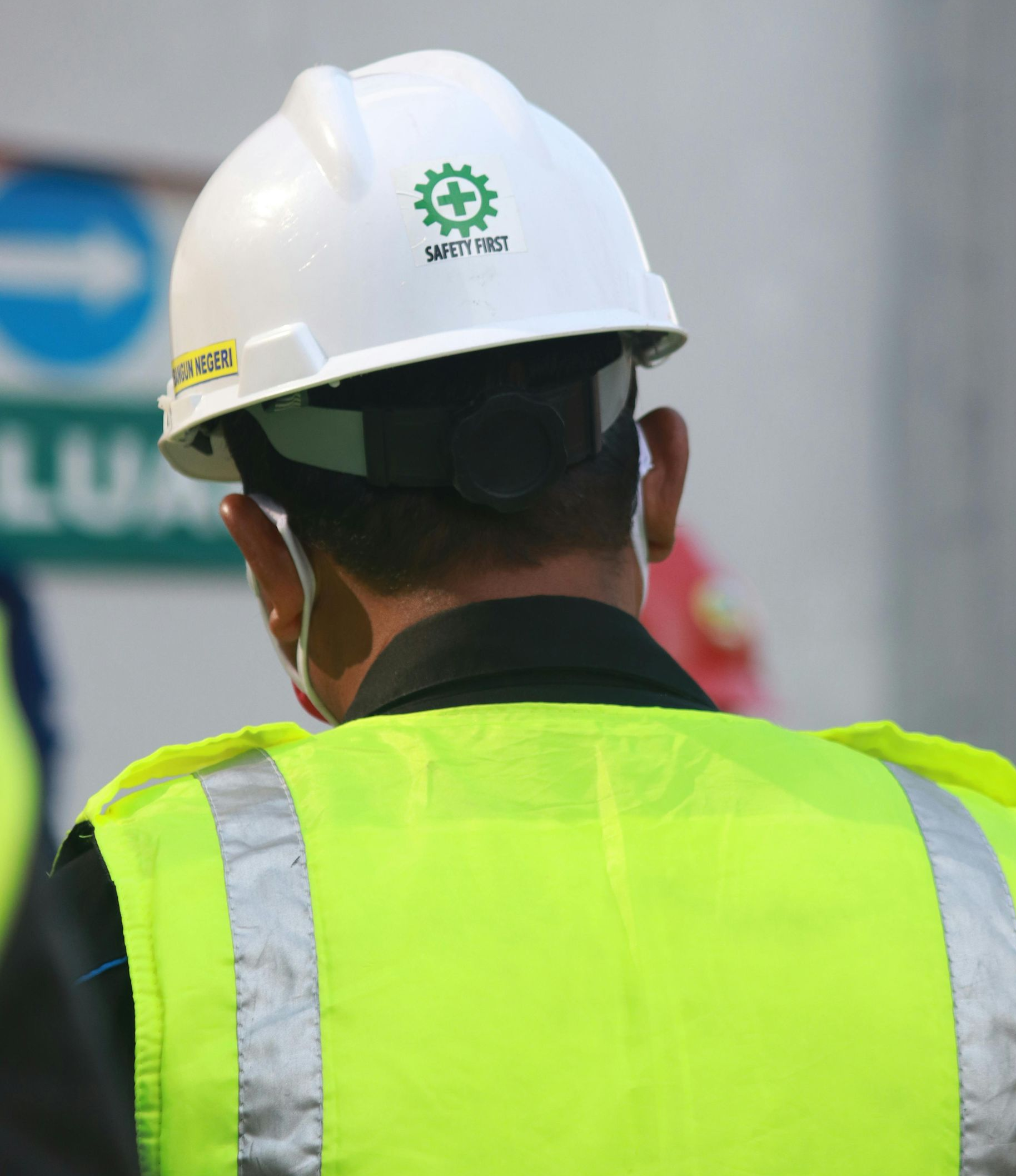 Person wearing white hard hat and neon vest, facing away.