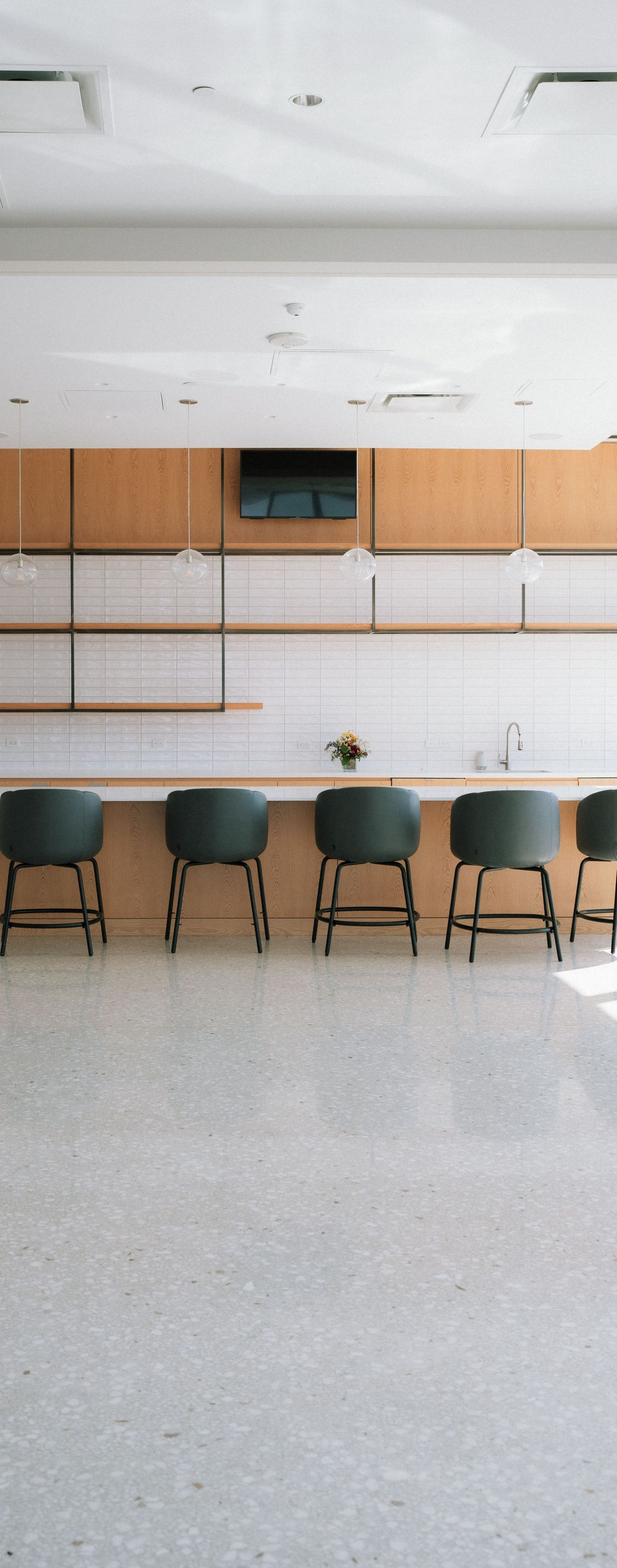 Bright empty room with a long counter, wall cabinets, and several chairs along the back wall