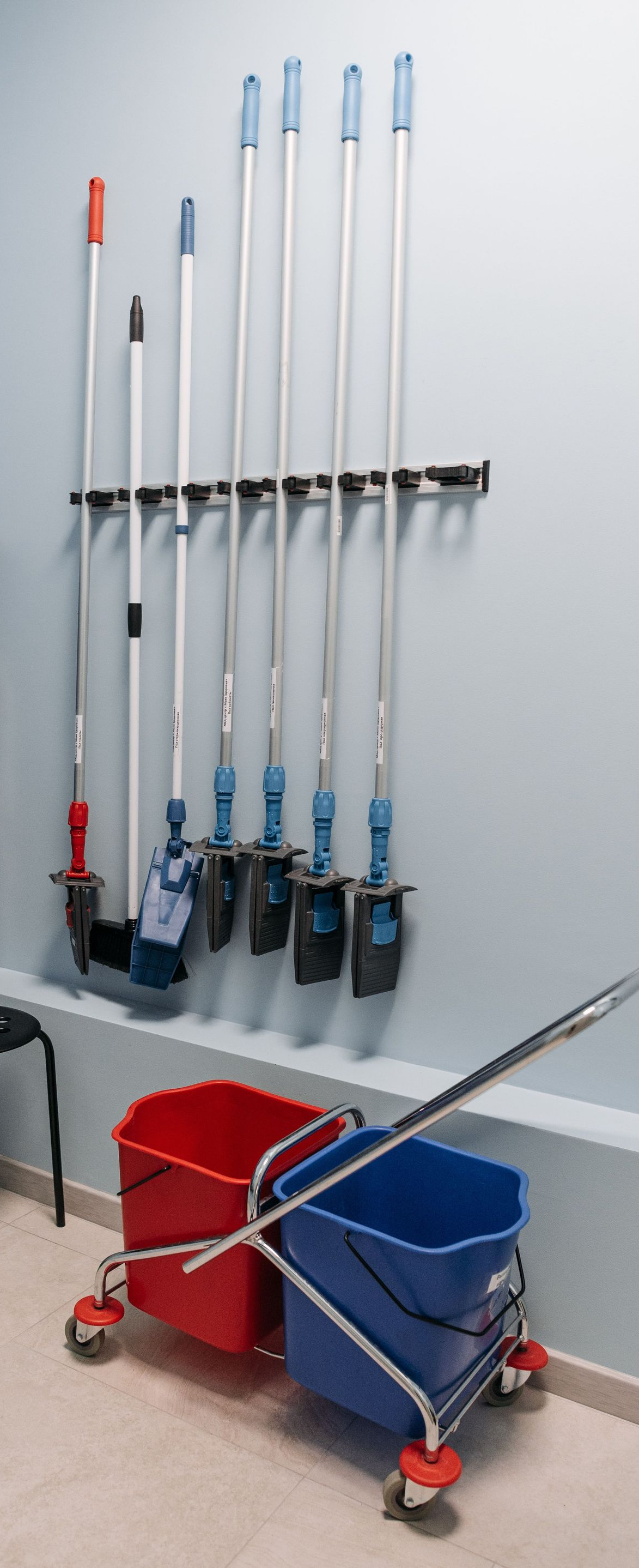 Janitorial closet with mops, brooms, cleaning supplies, and two red and blue mop buckets on carts