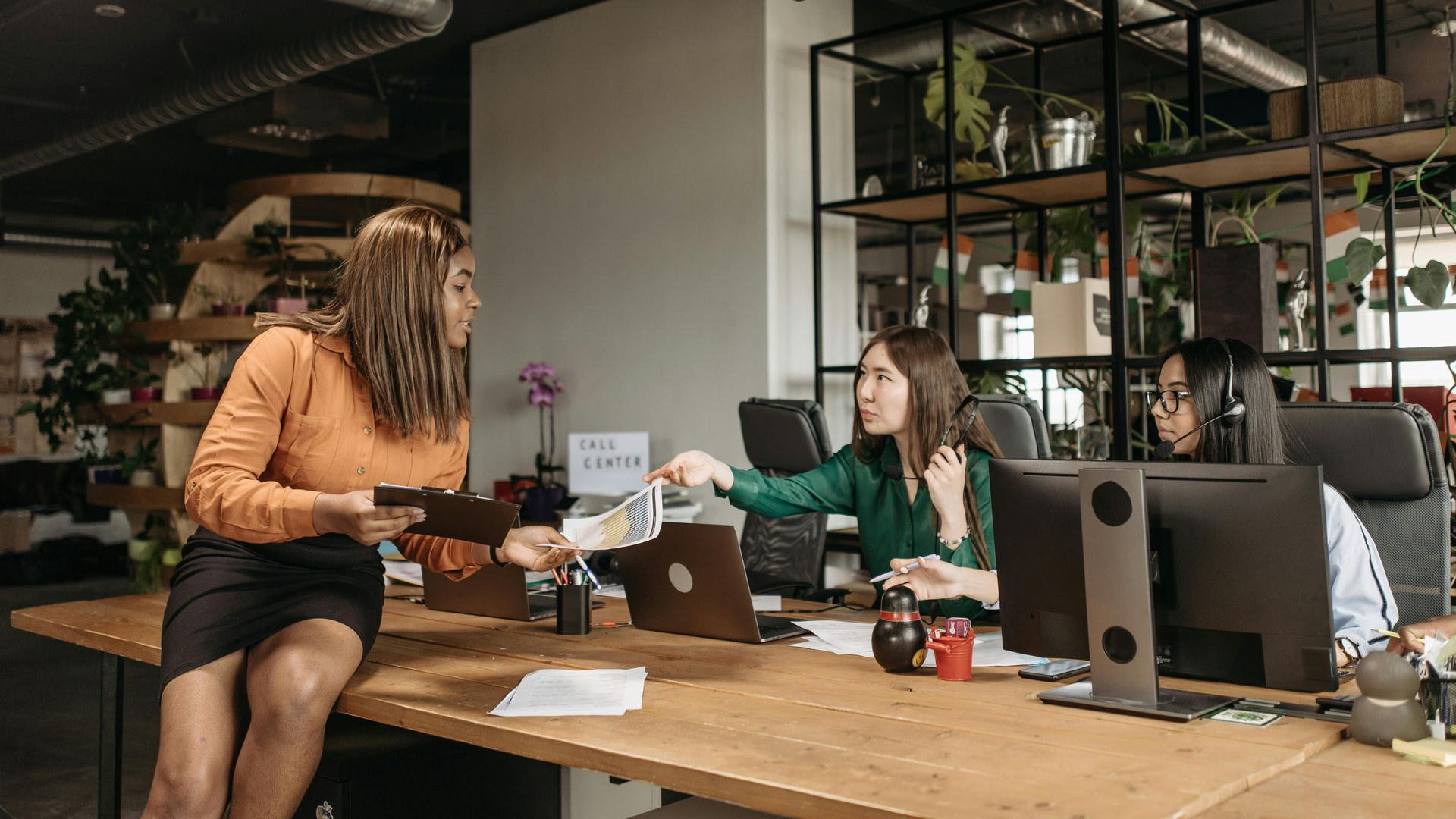 Two coworkers exchanging a package across a desk in a modern office