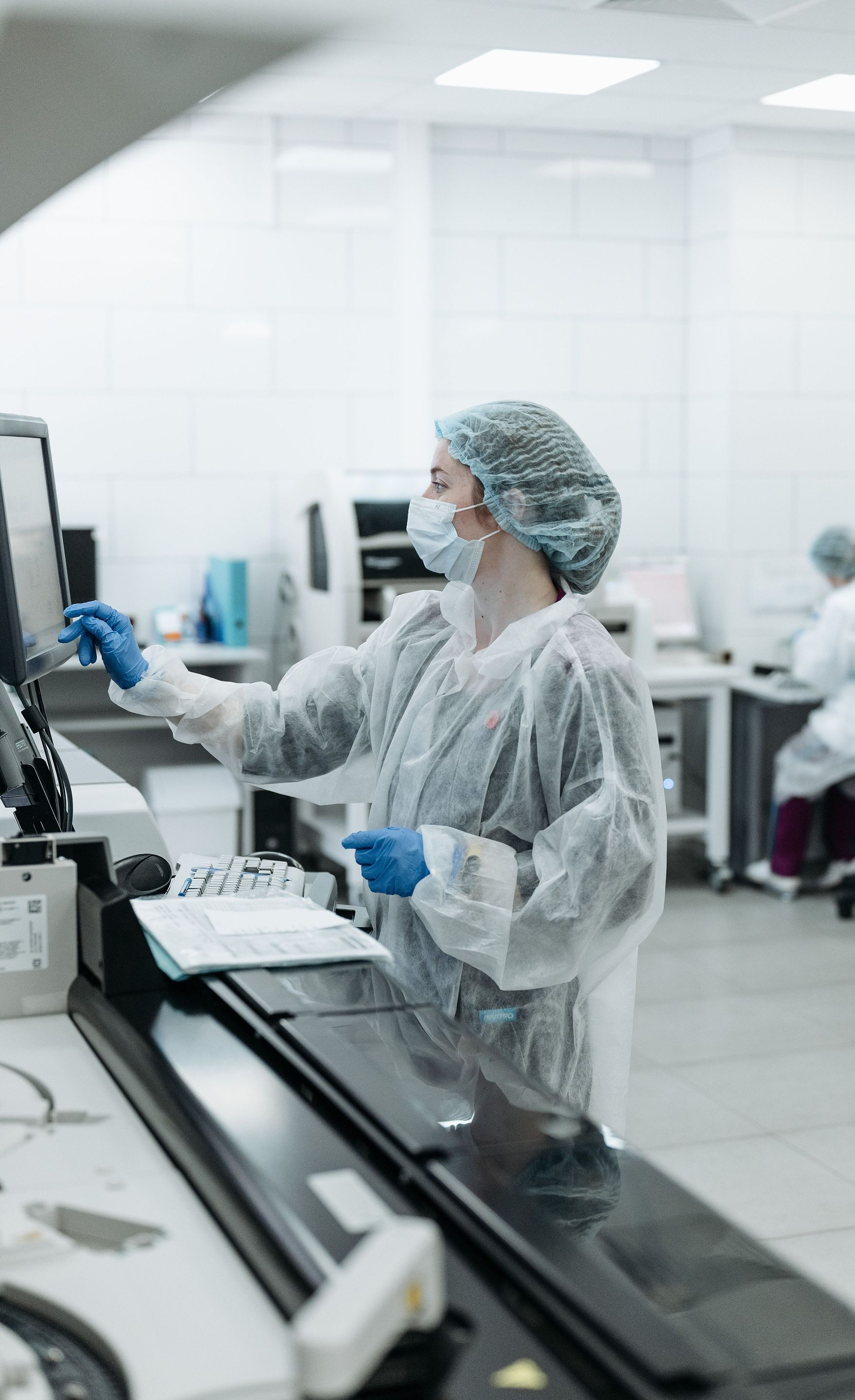 Technician in cleanroom gear using a computer in a sterile lab workspace