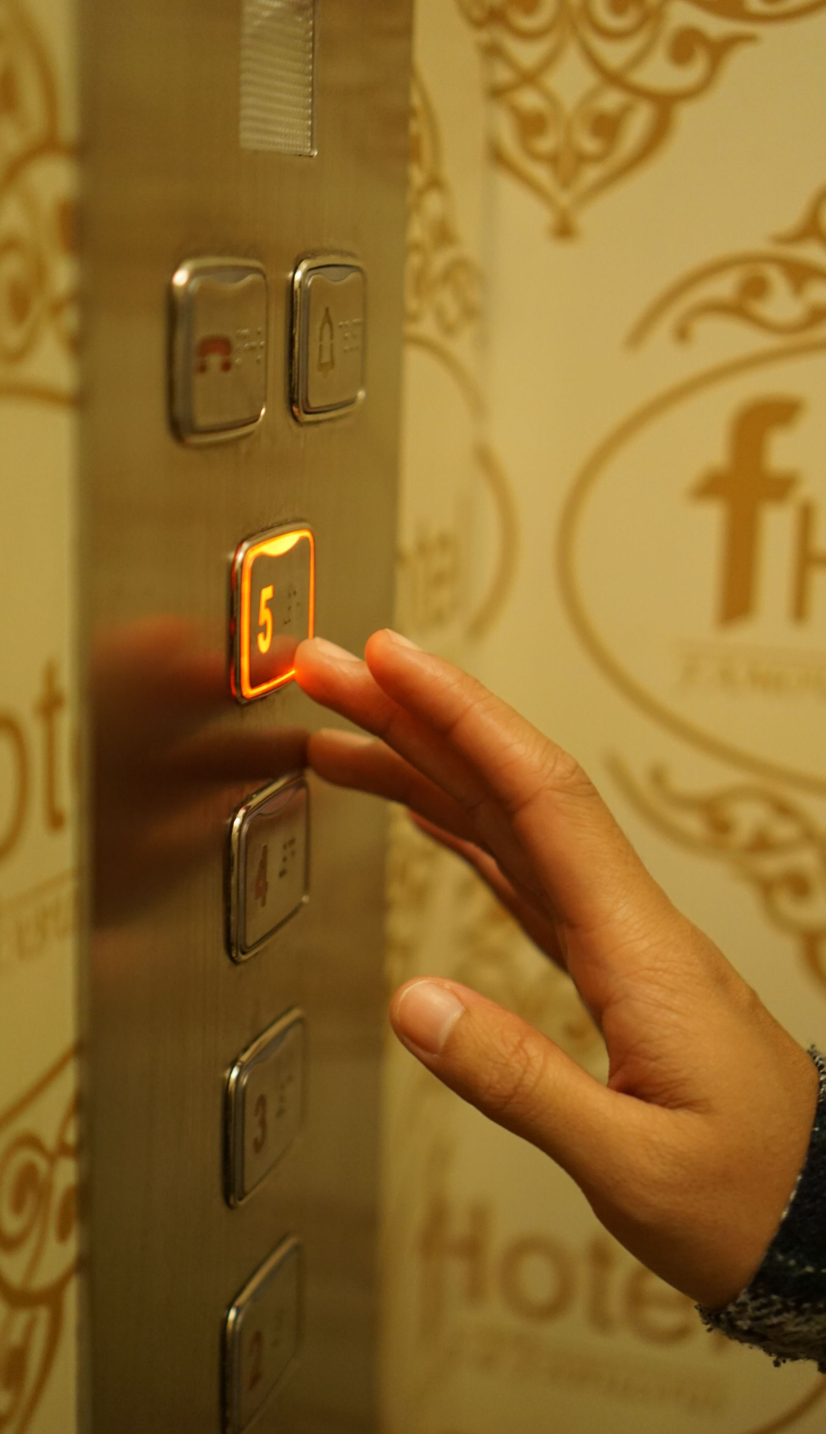 Hand pressing a lit elevator button in a gold-toned hotel interior