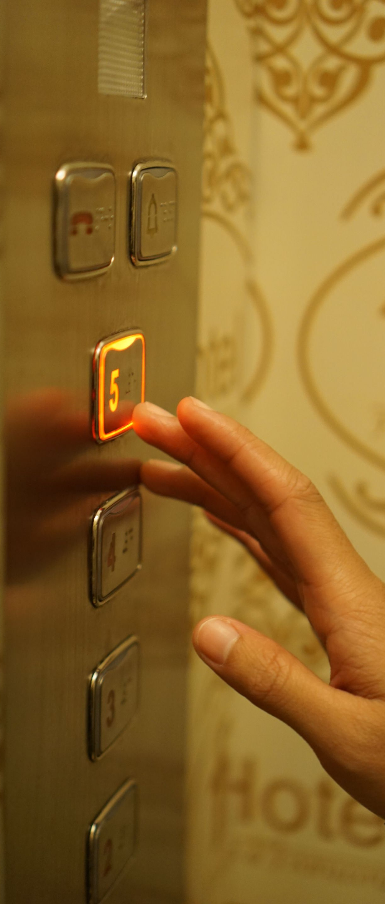 Hand pressing a lit elevator button on a panel with other buttons nearby