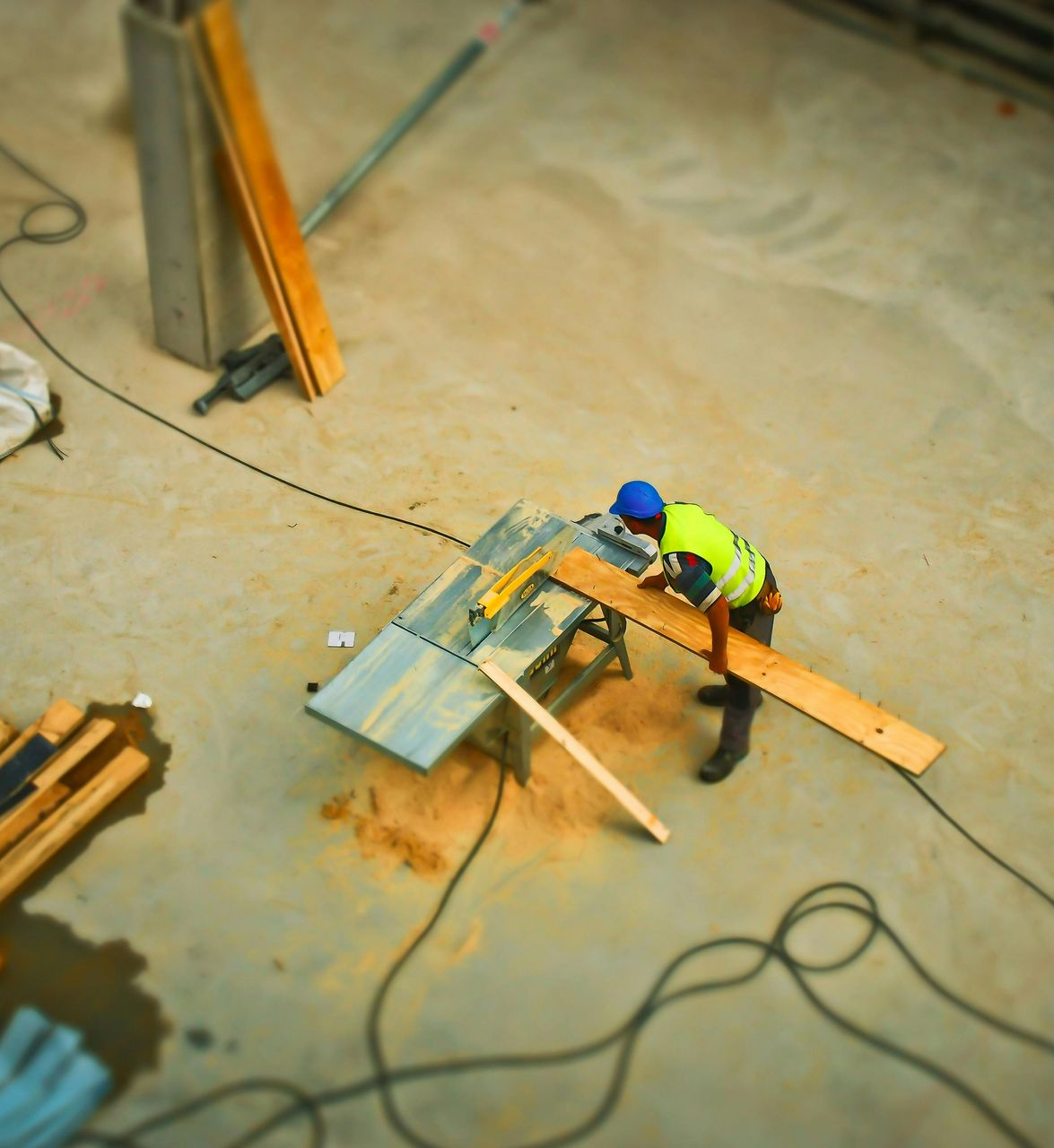 Construction worker using a saw to cut wood on a concrete surface, overhead shot.