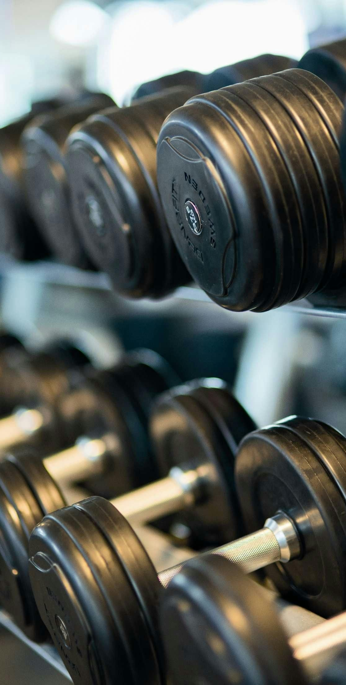 A rack of black dumbbells in a gym, with the foreground equipment in focus and the background blurred.