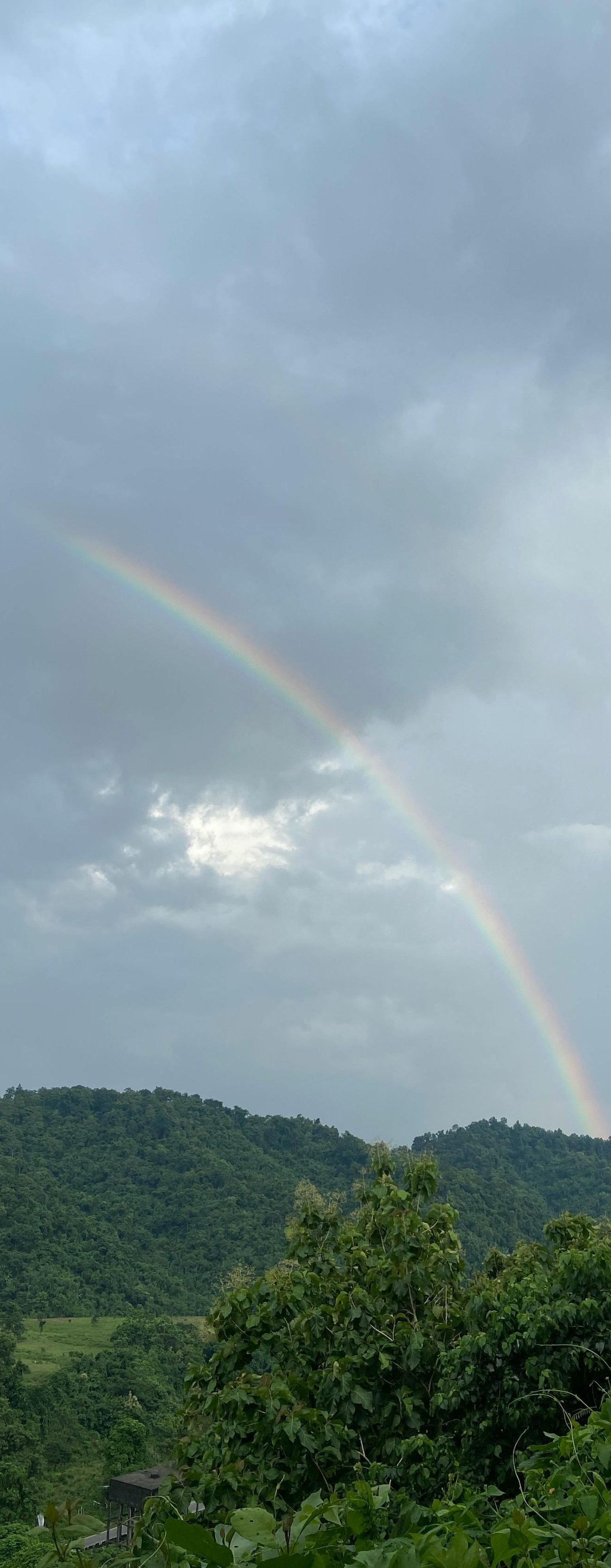 Rainbow over green hills beneath a cloudy sky