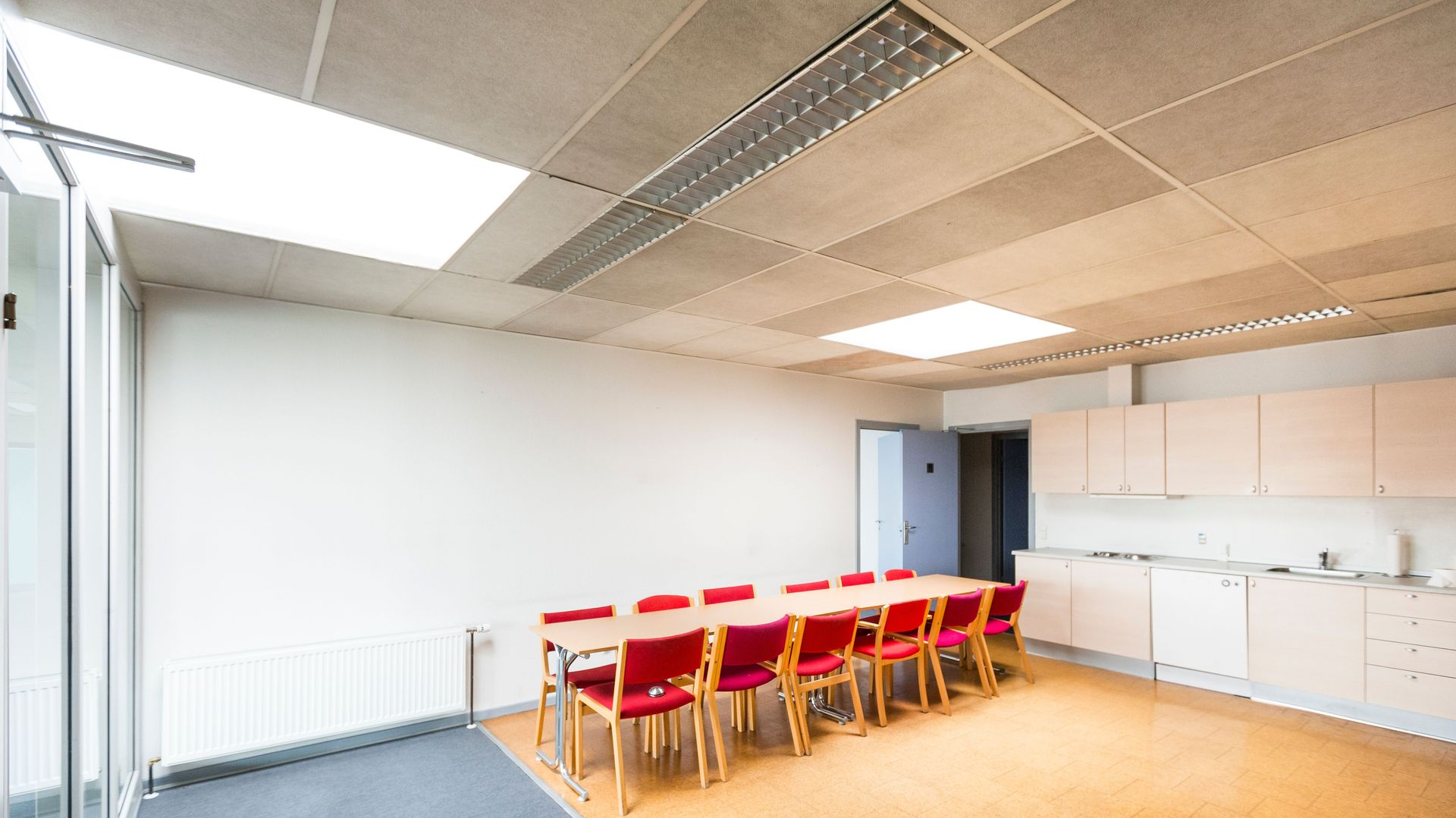 Bright empty meeting room with red chairs, long table, white cabinets, and large windows
