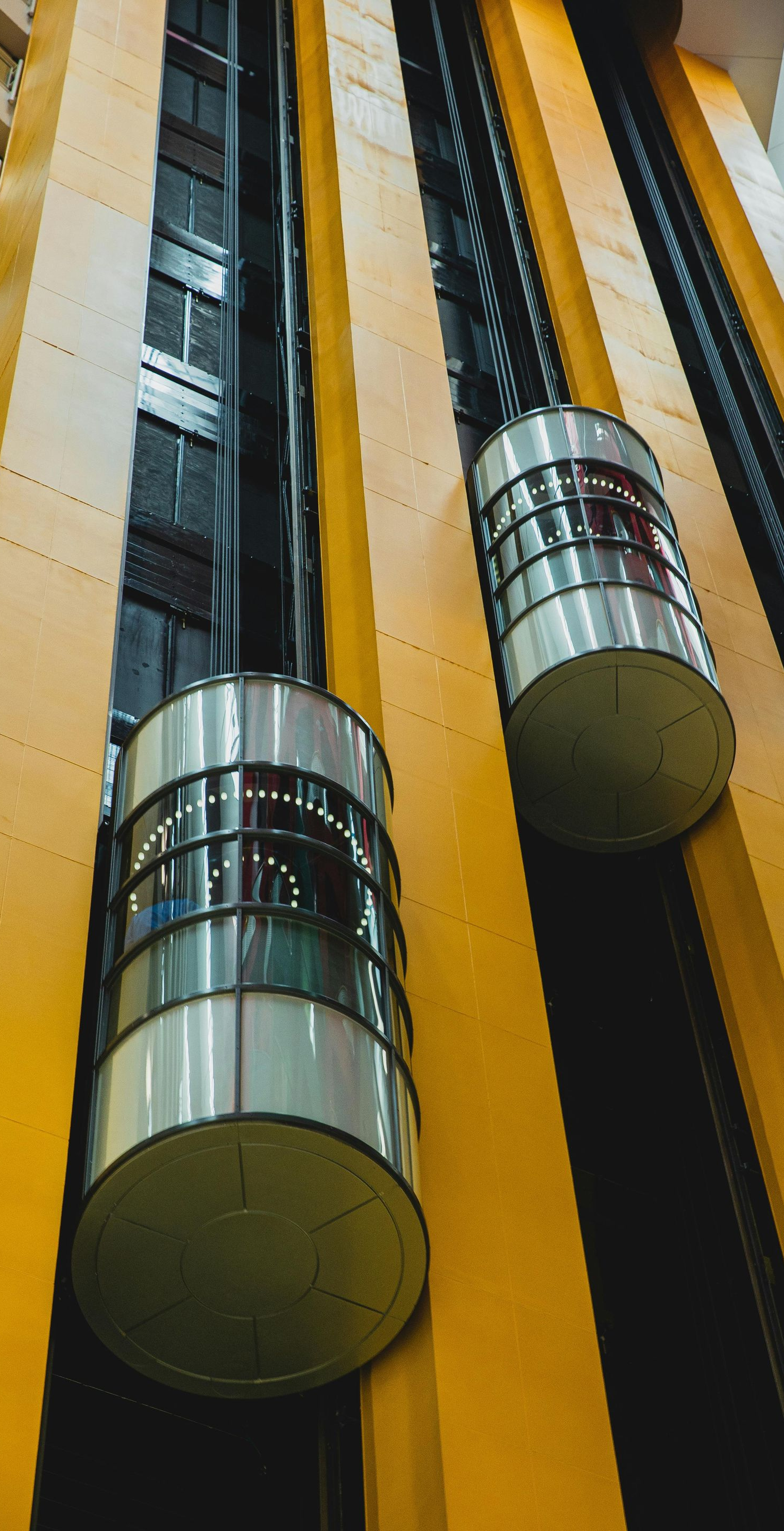 Two cylindrical elevators traveling in a tall, yellow-walled shaft.