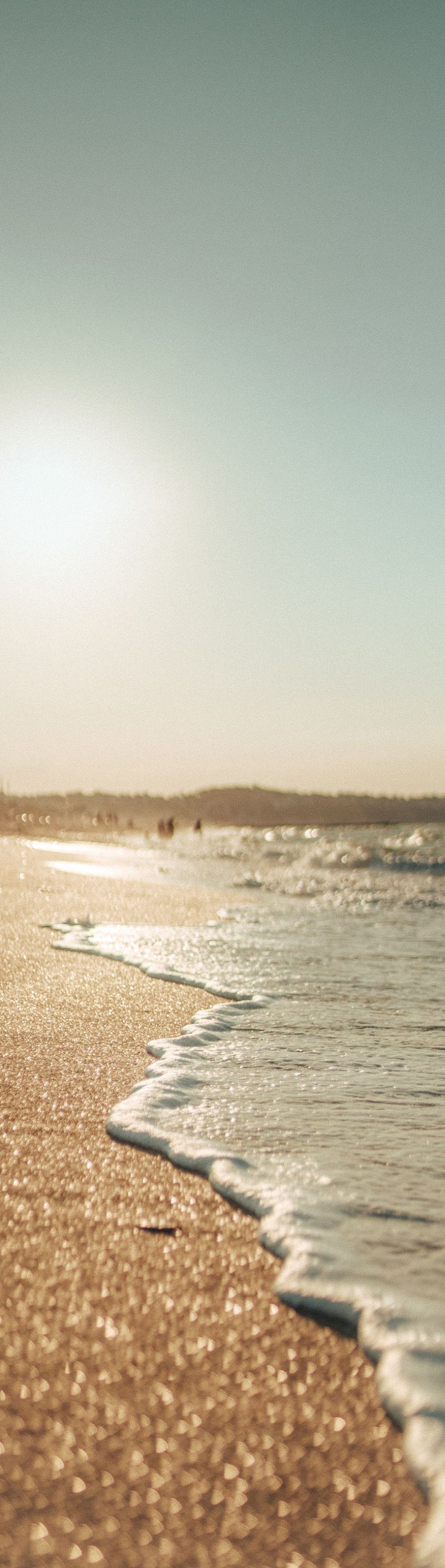 Sunny beach with gentle waves washing onto a golden shore at sunset
