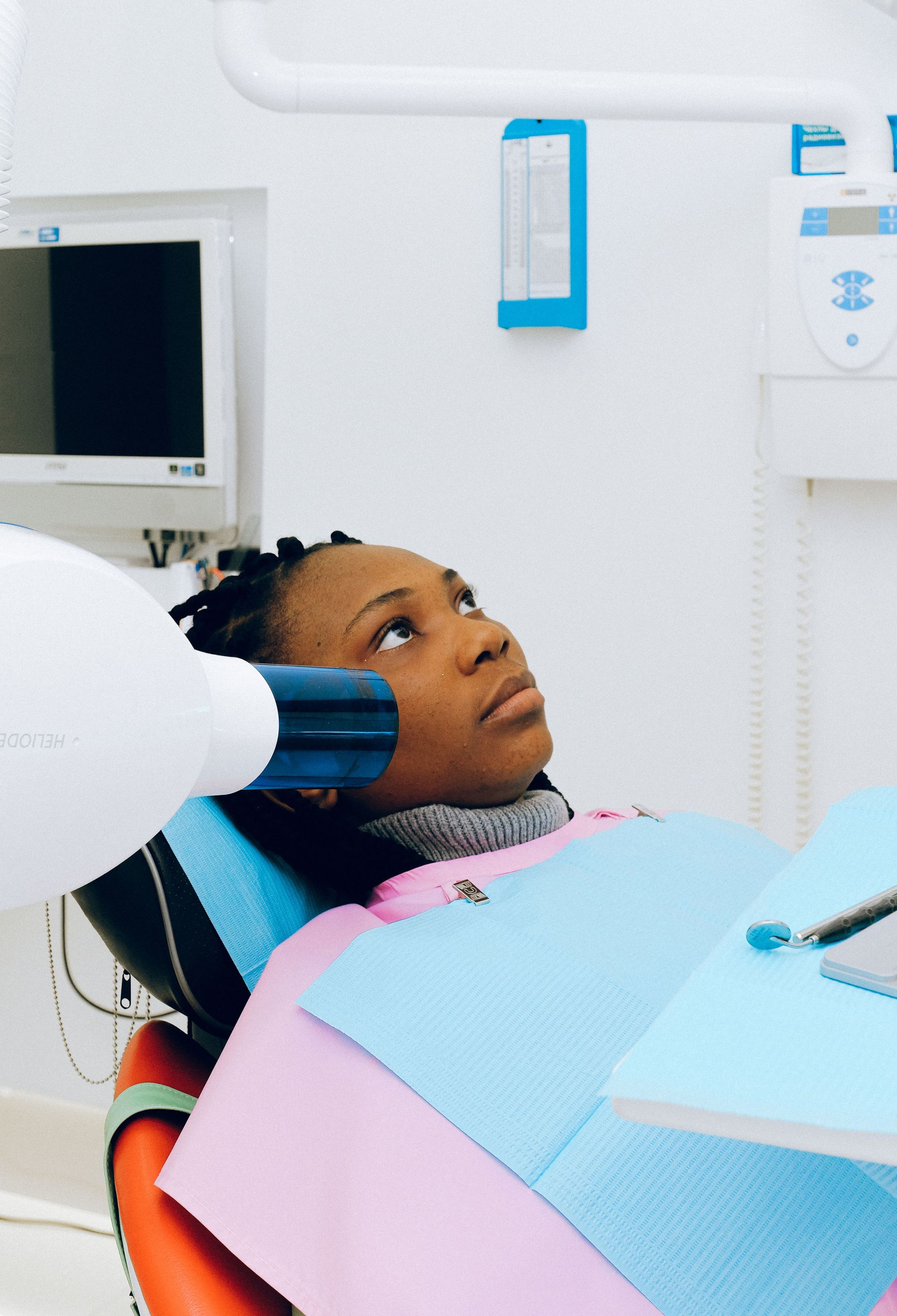 Patient reclining in a dental chair during an exam, with blue and pink dental bibs in a bright clinic