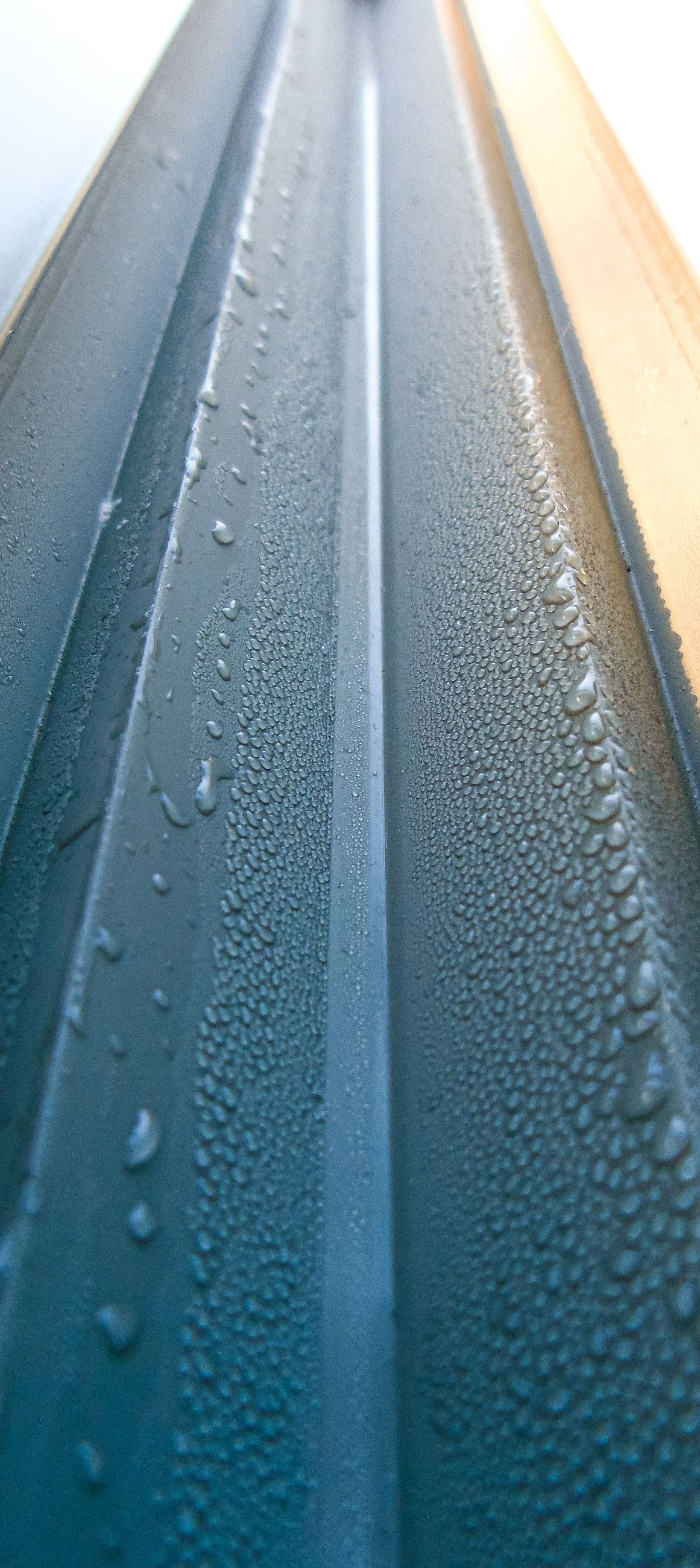 Close-up of a blue metal surface with water droplets and warm sunlight along the edge