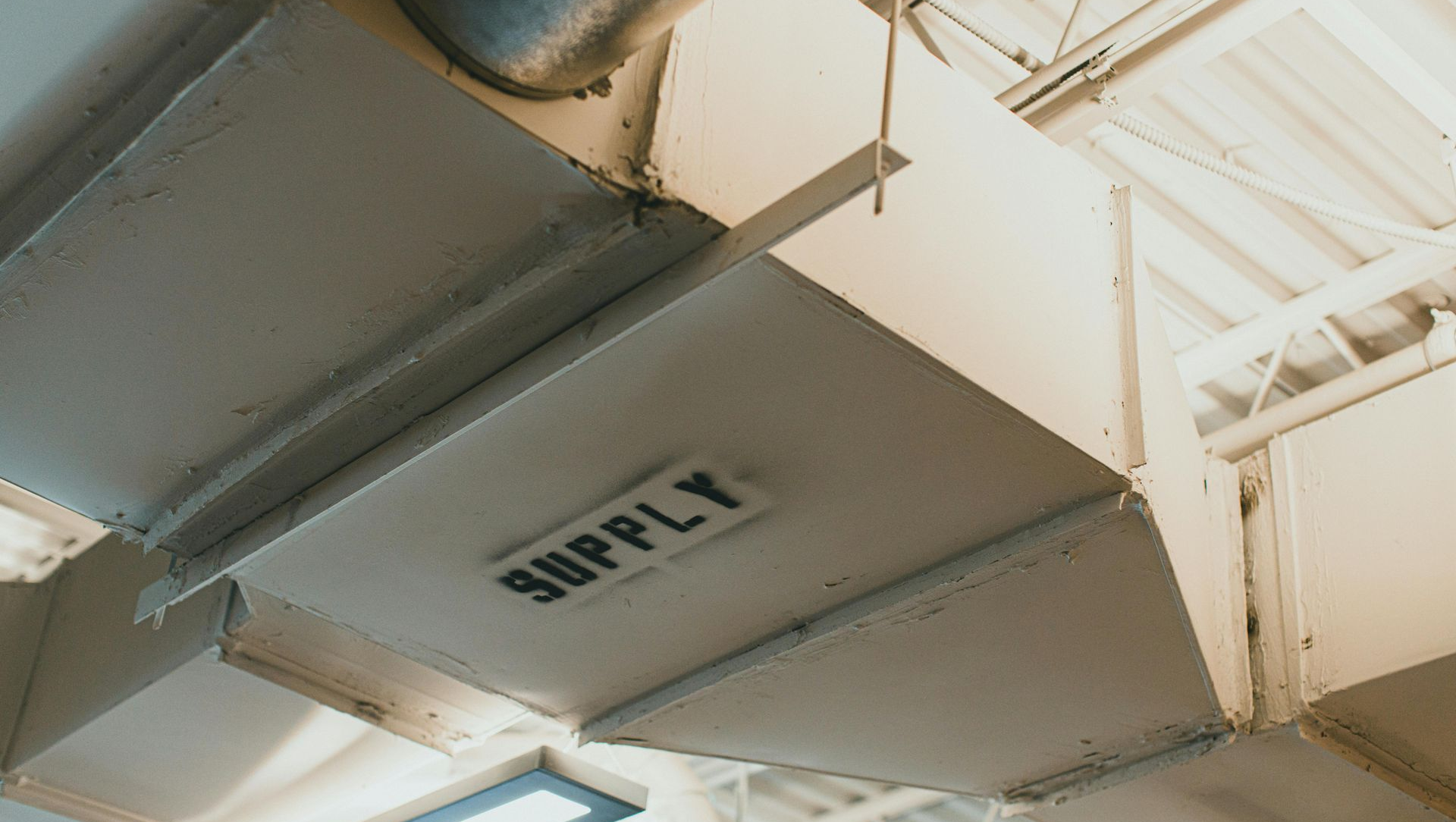 Ceiling vents and beams in a bright industrial interior, with one vent labeled “SUPPLY”