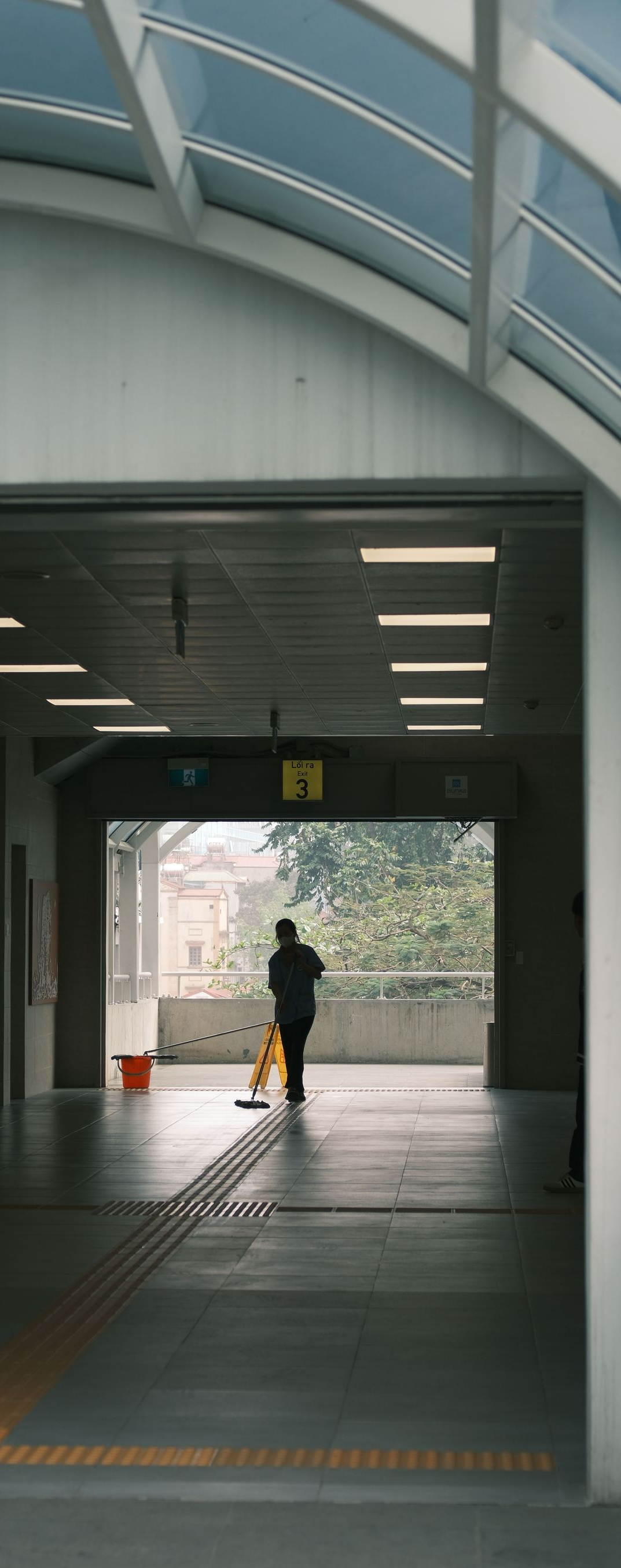 Covered walkway with a lone person standing at the far end, lit by overhead lights.