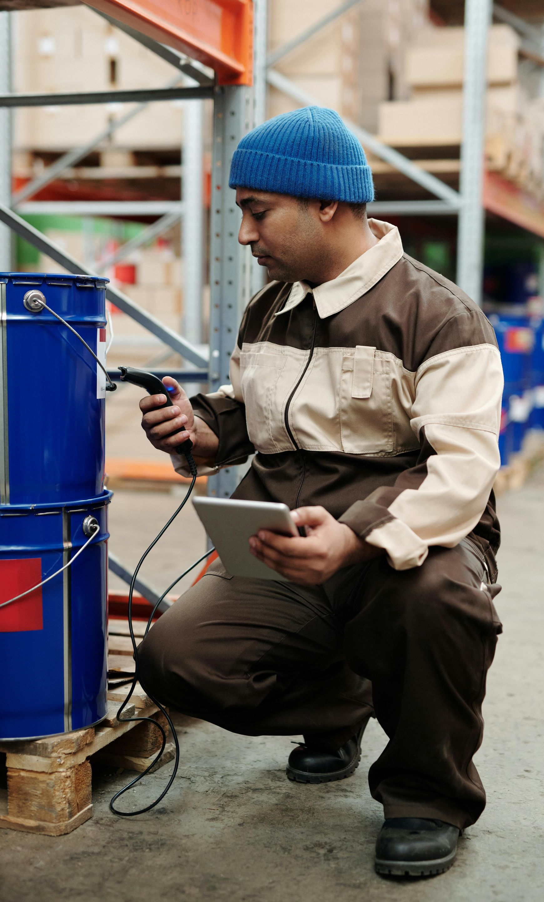 Warehouse worker scans a blue paint bucket with a handheld device, using a tablet.