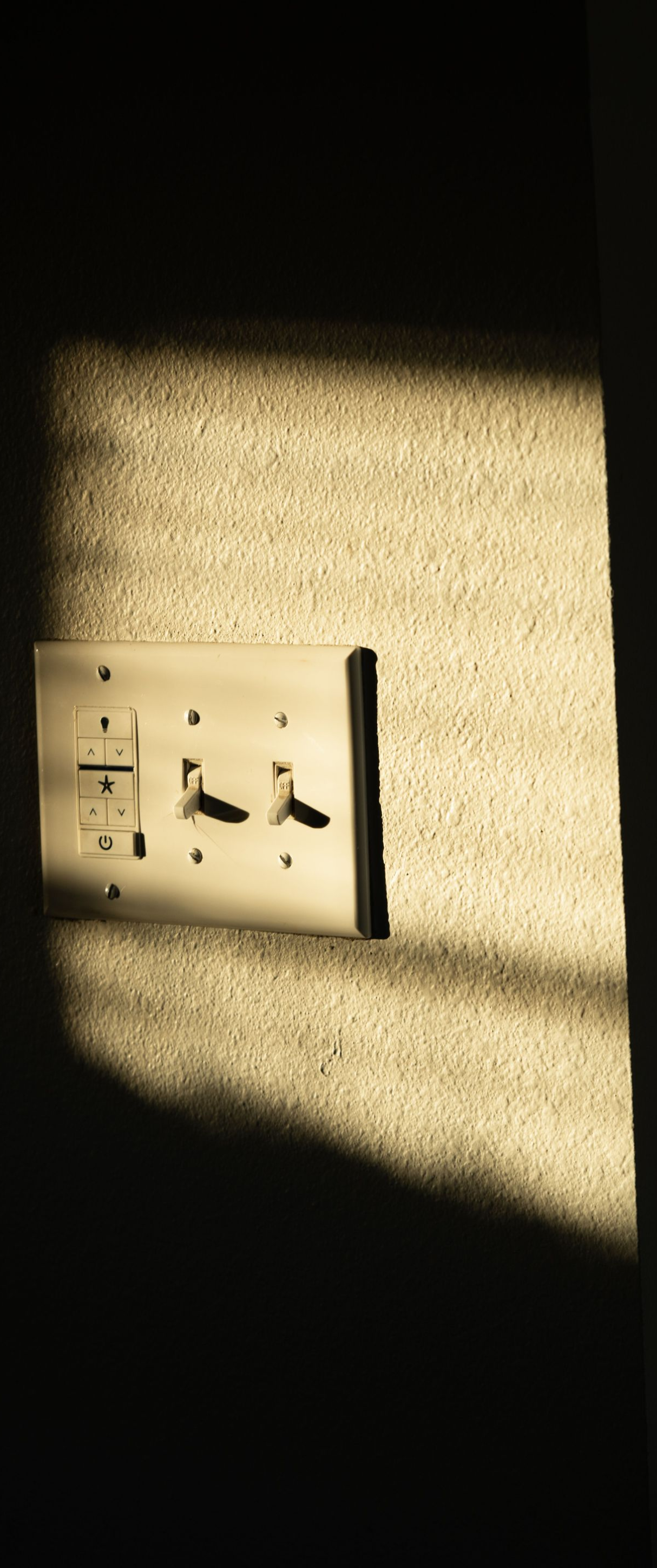 Sunlit wall with an electrical outlet and strong shadow across the surface