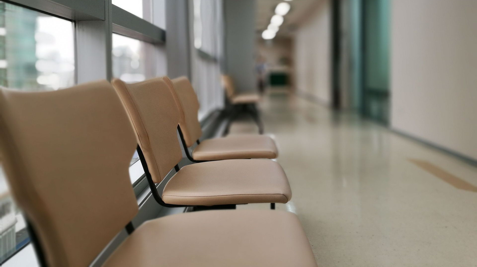 Empty tan chairs in a bright hallway with windows and a blurred corridor background