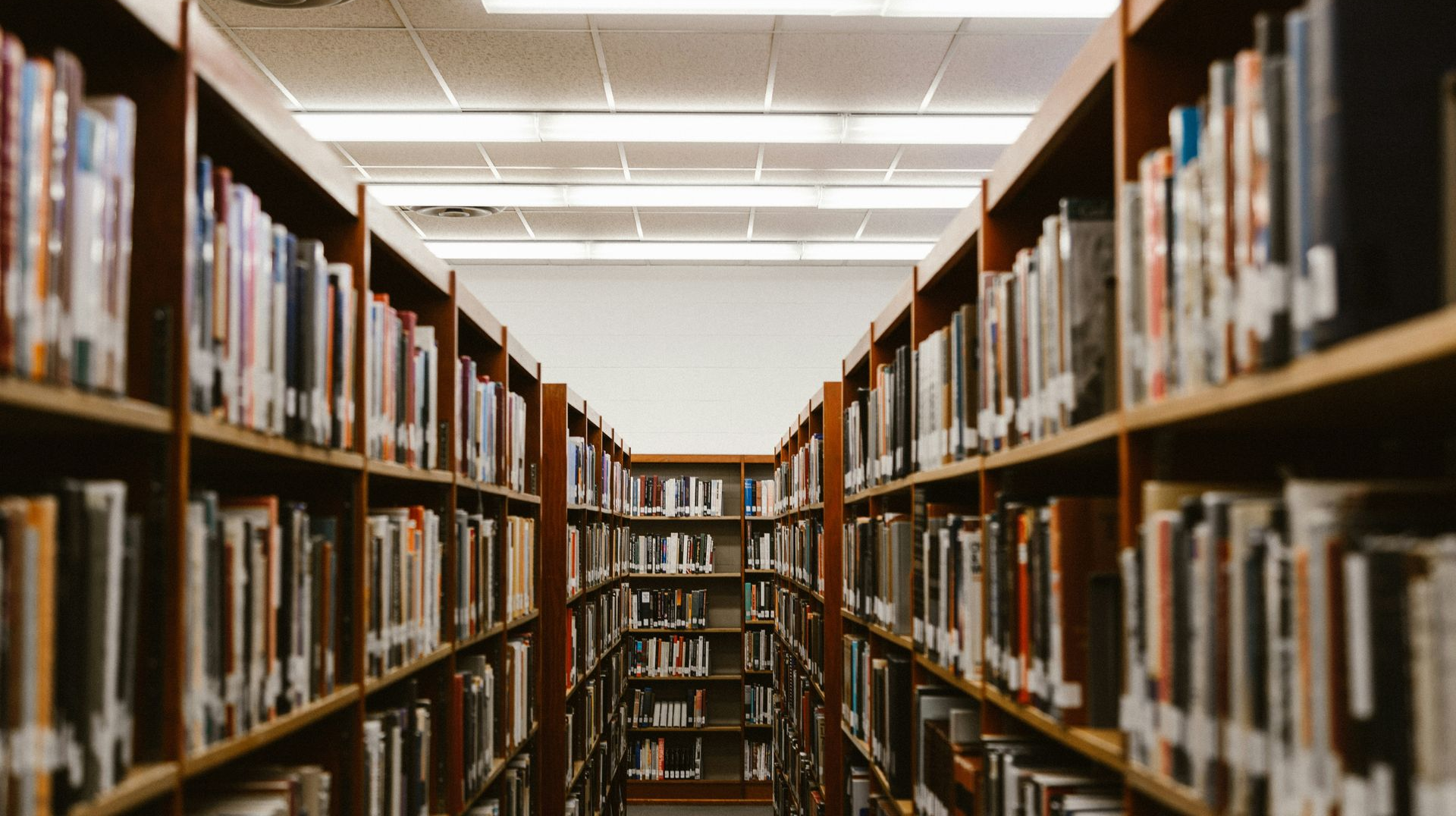 Bookshelves full of books in a library, view down a central aisle towards bright light.
