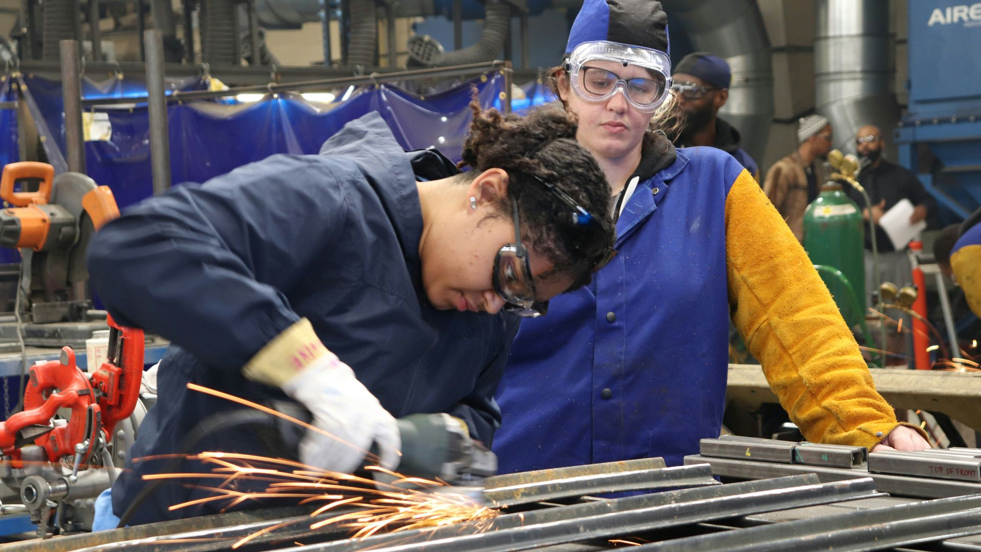 Two workers in safety gear welding metal in a workshop, with bright sparks flying.