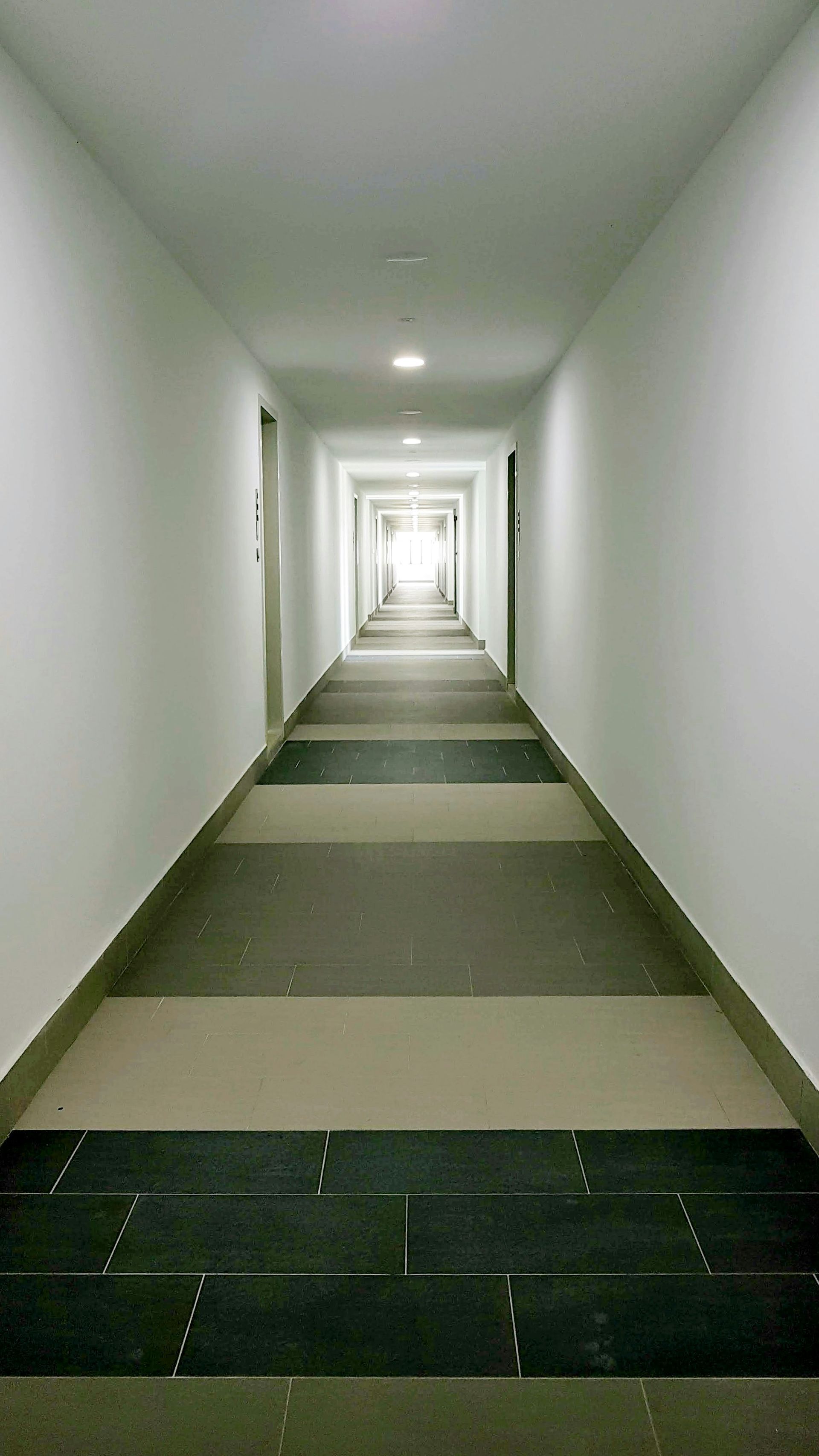 Long, narrow hallway with white walls and a patterned floor.