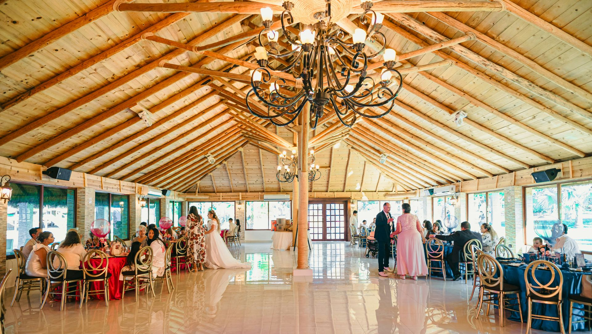 A bright indoor event hall with a vaulted wooden ceiling, a large chandelier, and guests seated at tables.