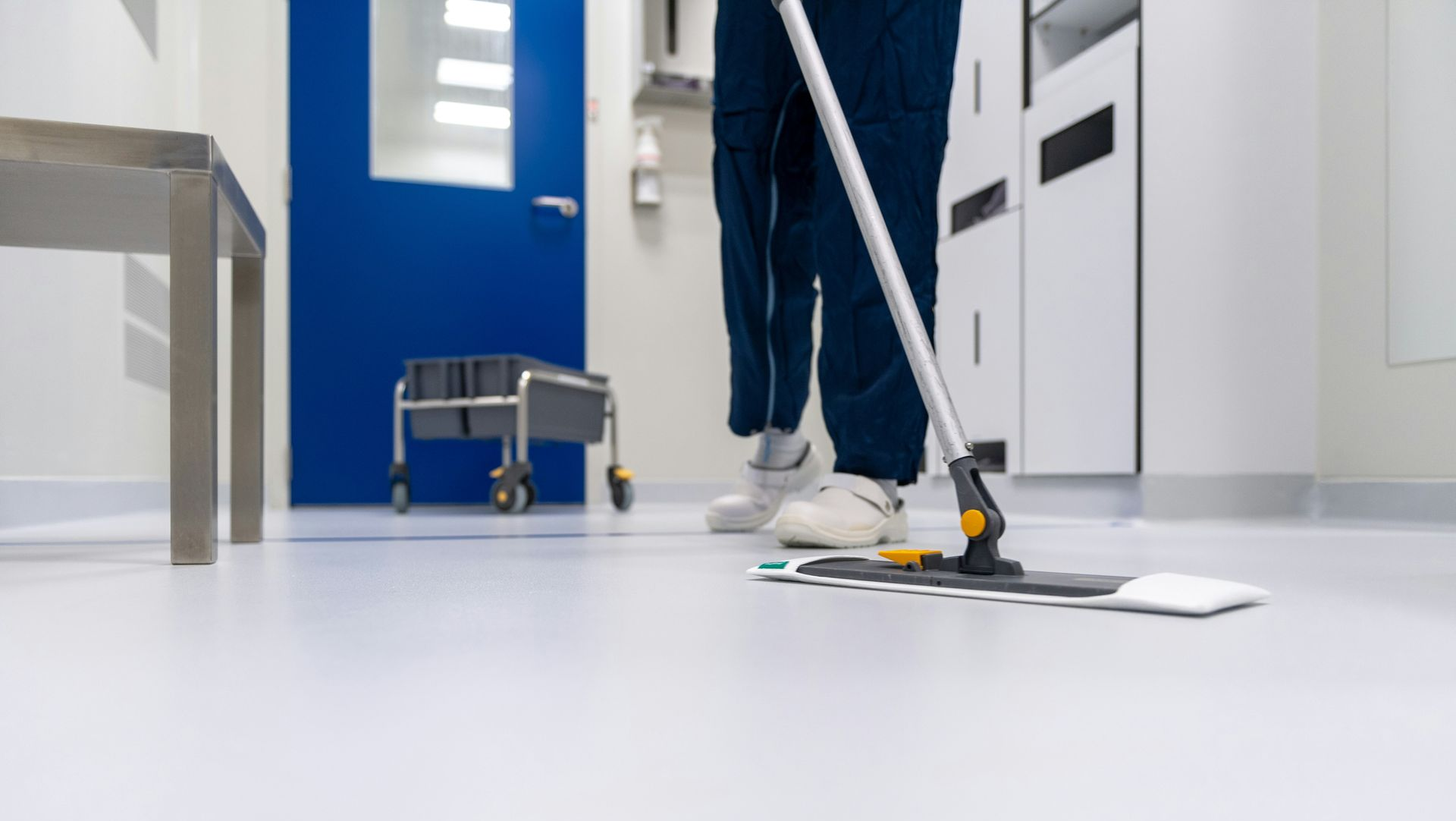 Janitor mopping a white floor in a bright hallway with blue walls