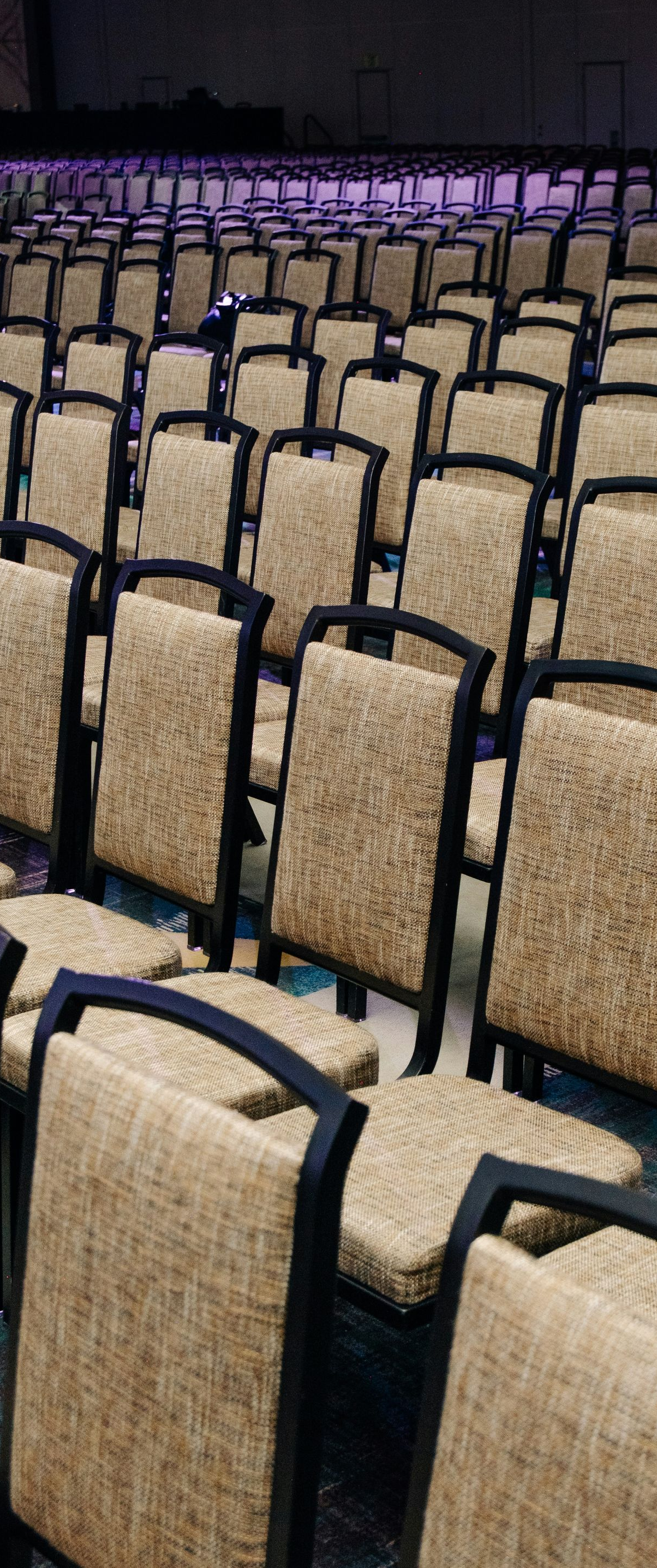 Rows of empty, beige-upholstered banquet chairs arranged in a large conference hall.