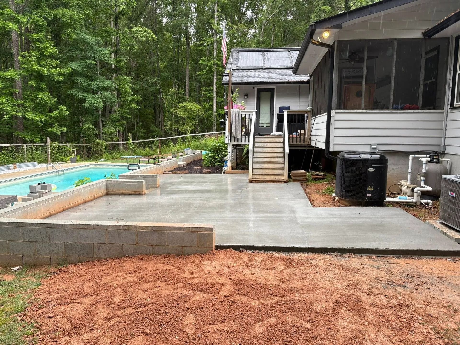 Backyard patio with concrete pool deck beside a house and wooded yard