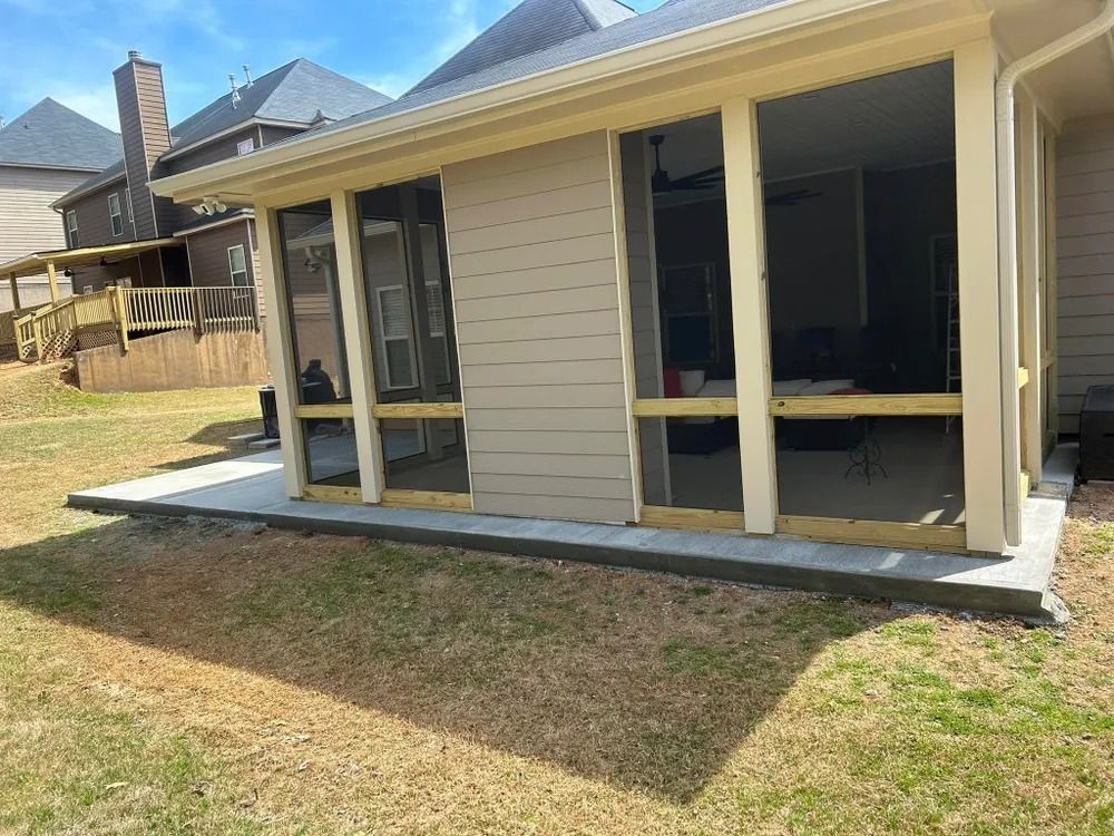 Covered backyard patio with beige siding, white posts, and a concrete slab beside a grassy yard.