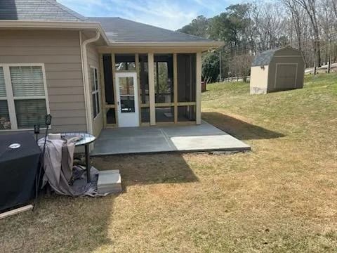Backyard patio with screened porch and concrete slab beside a beige house, grassy yard and small shed in background