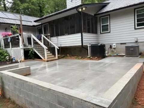 Concrete patio under construction beside a house with white siding and porch stairs.