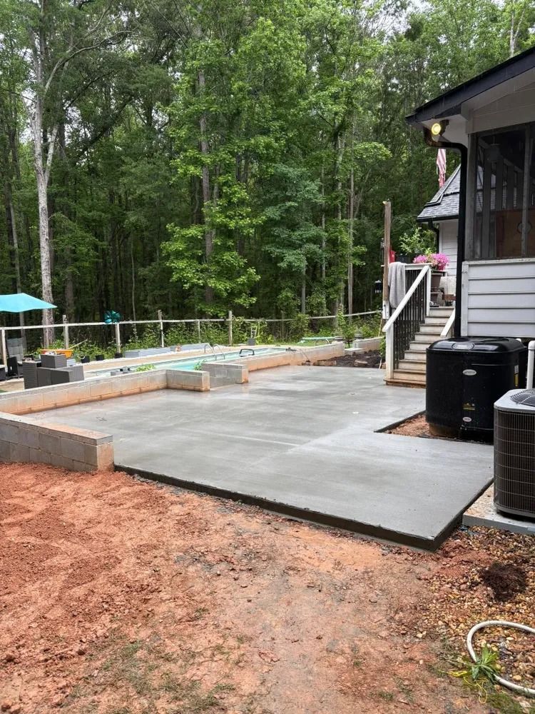 Backyard patio under construction with concrete slab, retaining blocks, and steps beside a house and trees