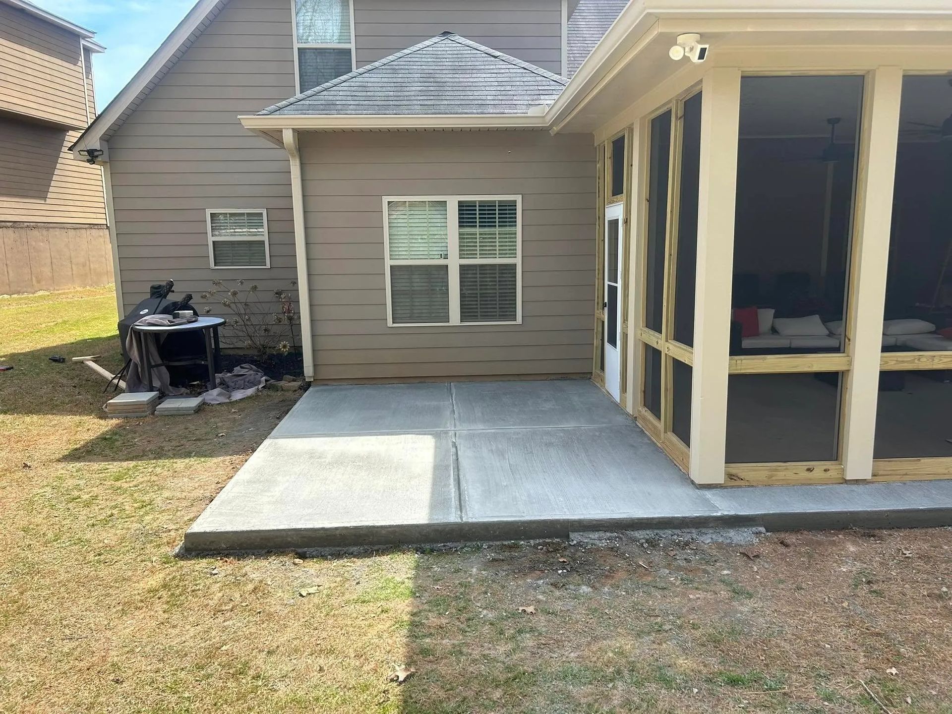 Backyard patio with concrete slab and screened porch beside a tan house