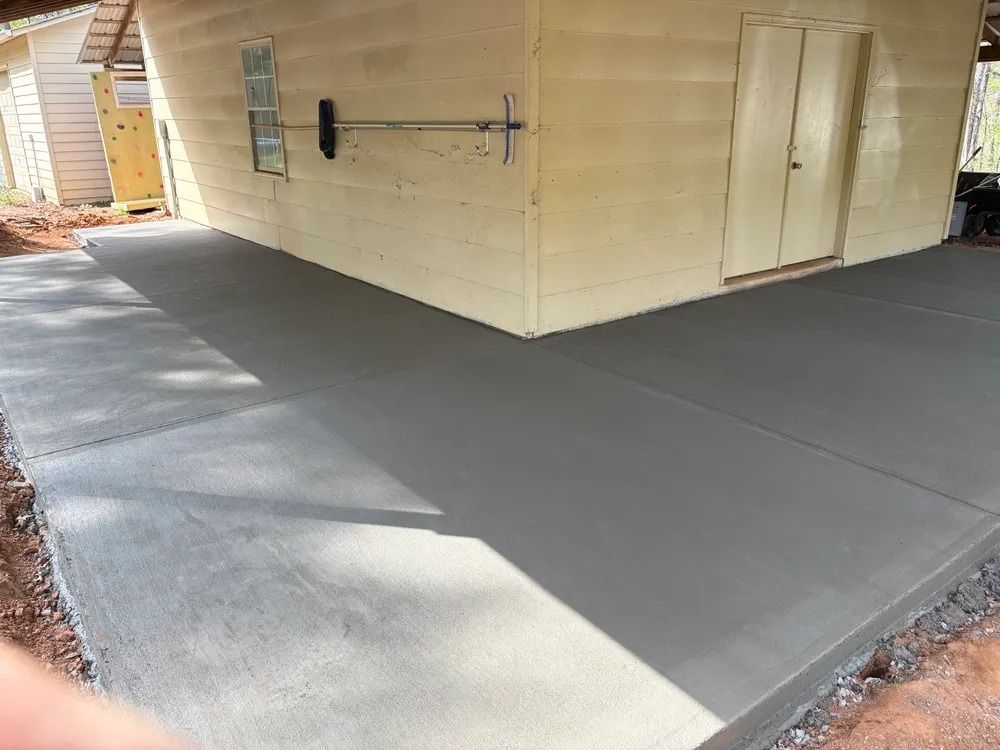 Fresh gray concrete patio beside a beige house, with a shadowed walkway and exterior door.